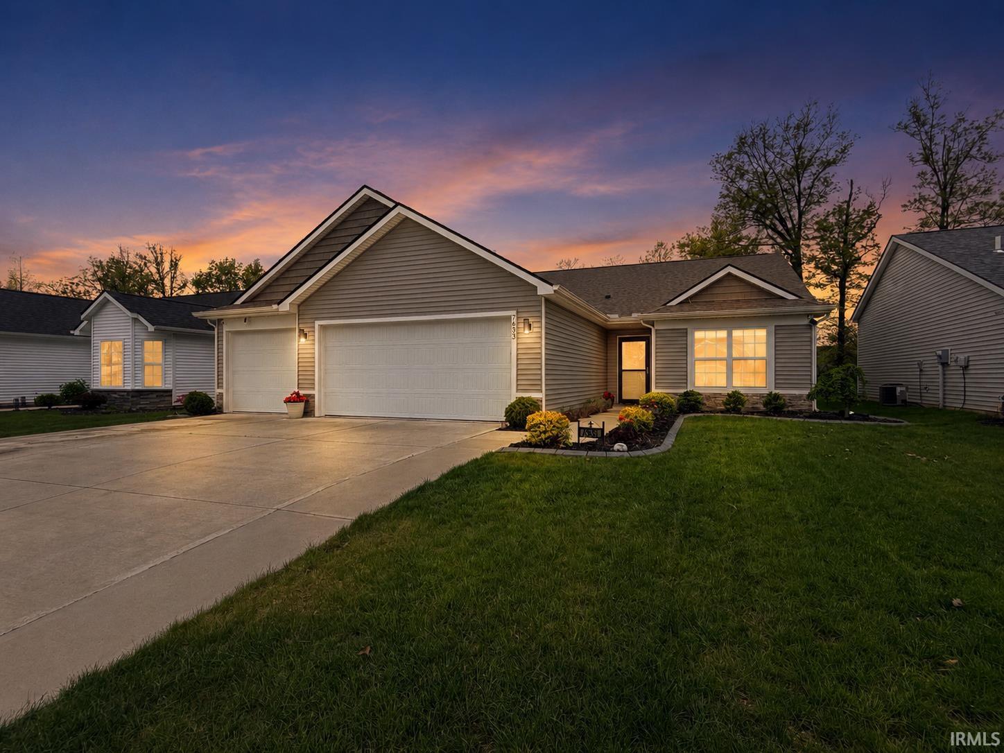 Ranch-style residence featuring a two-car garage, gray horizontal siding, stone accents, and dark trim