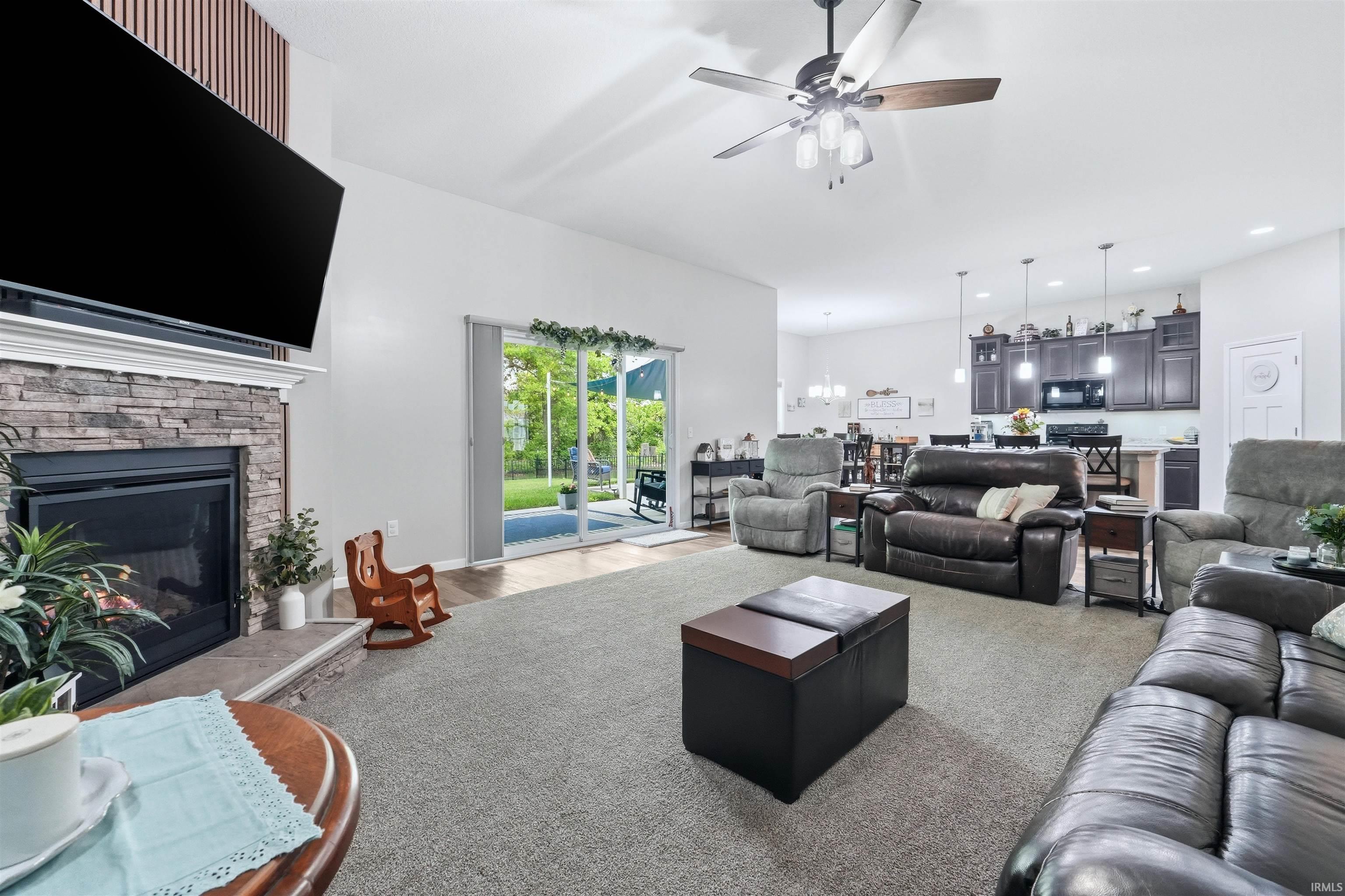 Living room featuring a stacked stone fireplace with hearth, a ceiling fan with integrated lighting, and direct access to the outdoor space through sliding glass doors