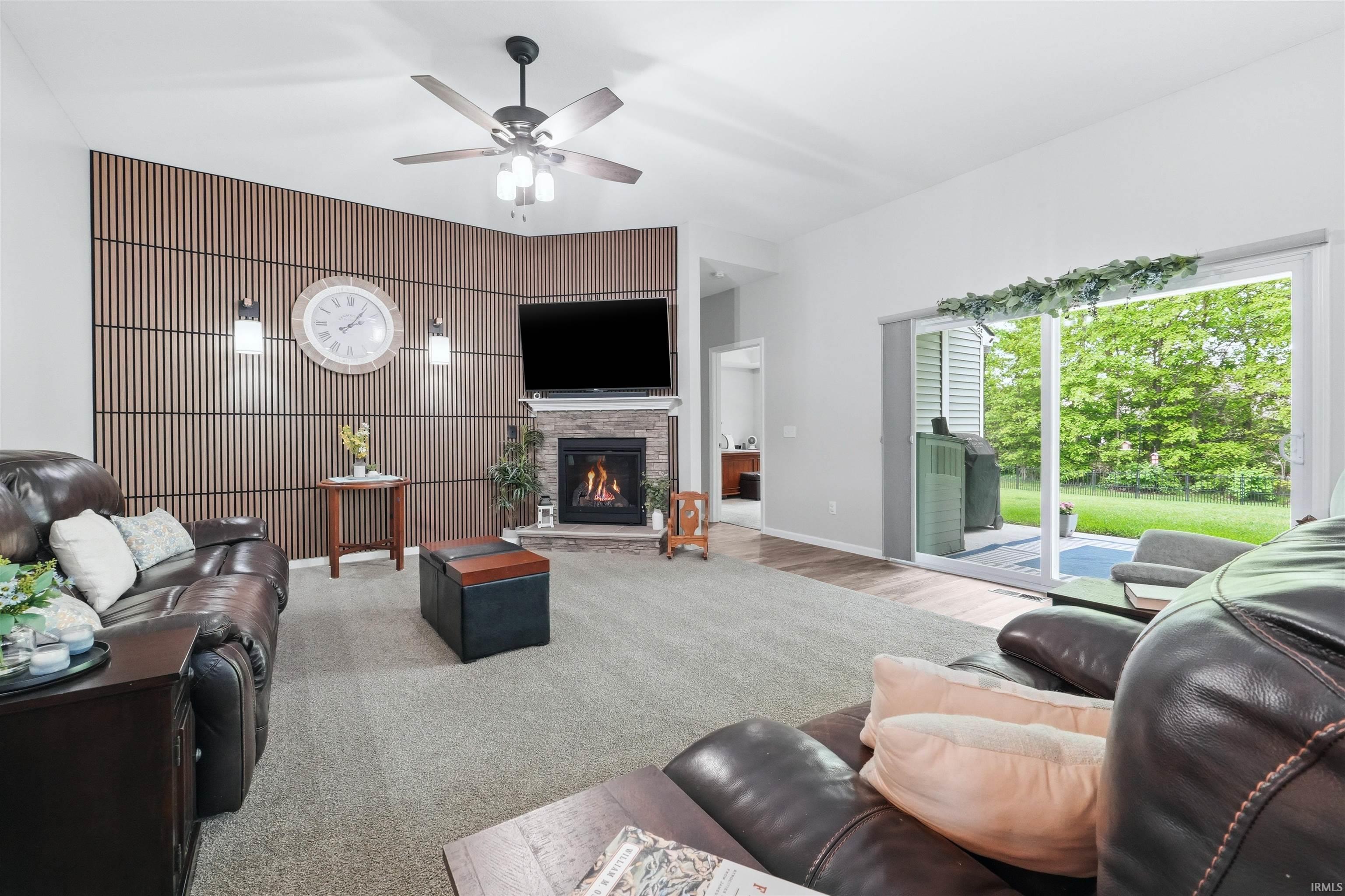 Living room featuring a stacked stone fireplace, wood slat accent wall, and ceiling fan with integrated lighting