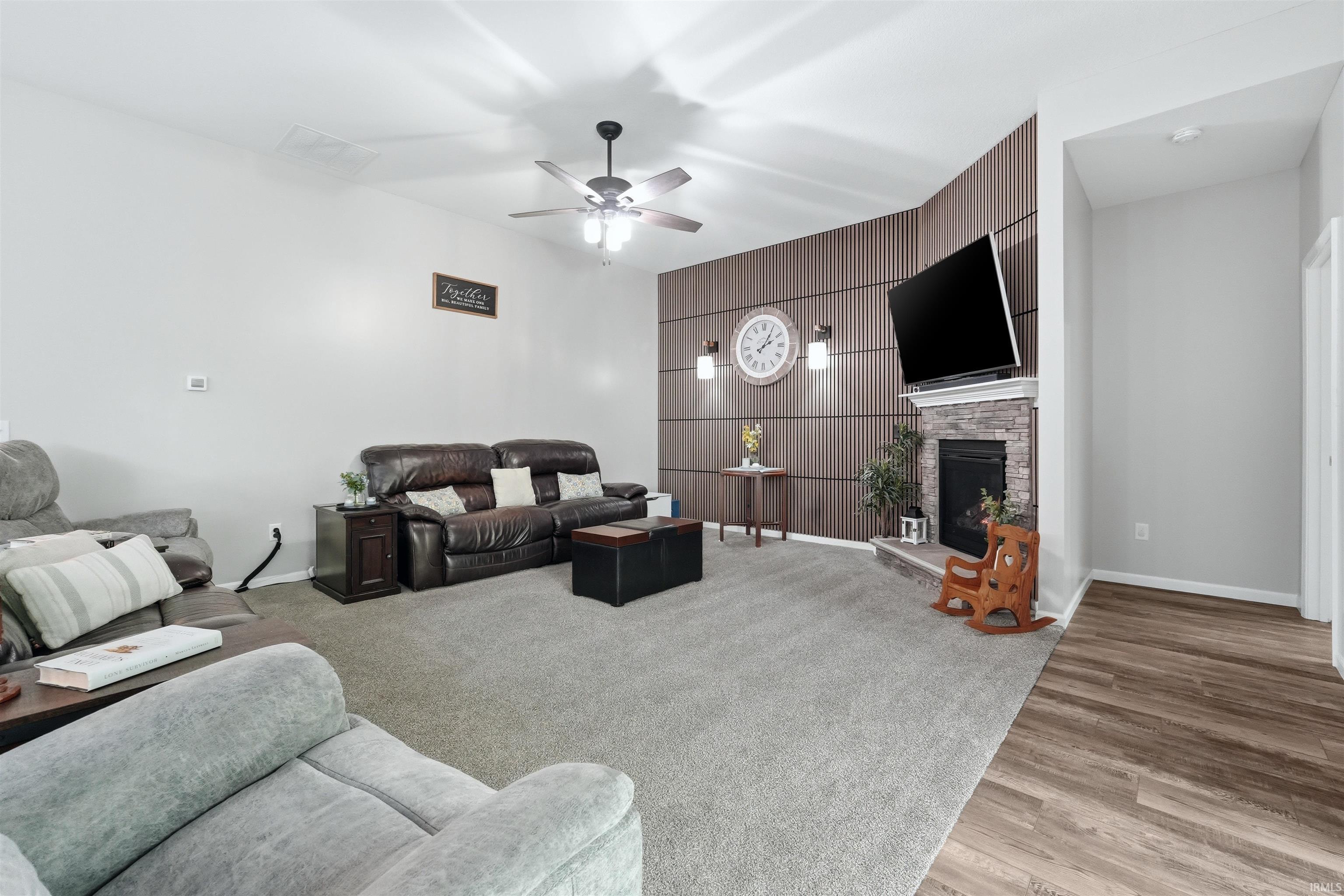 Living area featuring a stone-clad fireplace, wood-finish accent wall, and a ceiling fan with integrated lighting