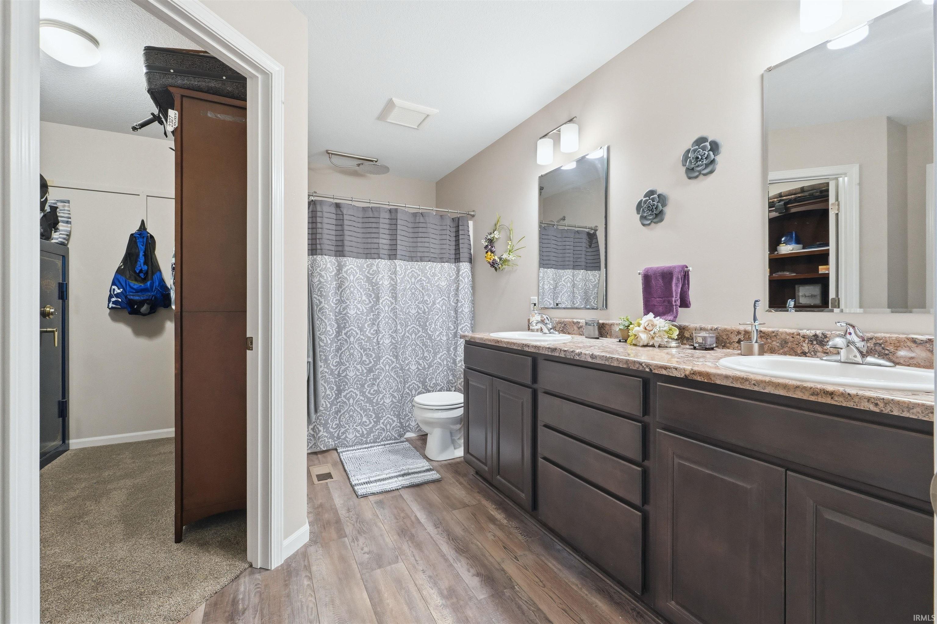 Spacious bathroom featuring a double vanity with two undermount sinks, wood-finish flooring, a combination shower and tub, and a separate closet with built-in shelving