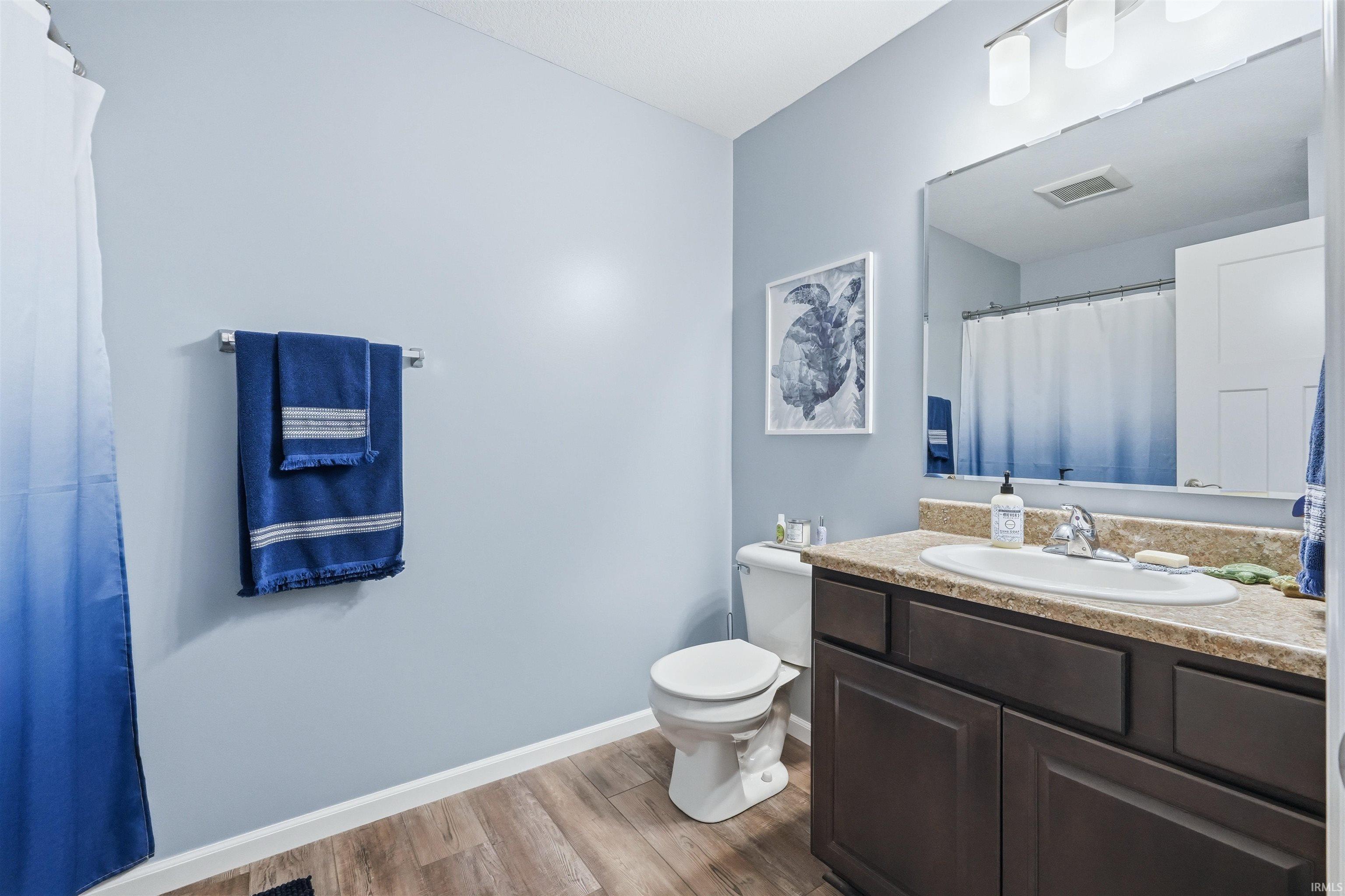 Bathroom featuring wood-finish flooring, a dark wood-finish vanity with an integrated sink, and a light-toned countertop