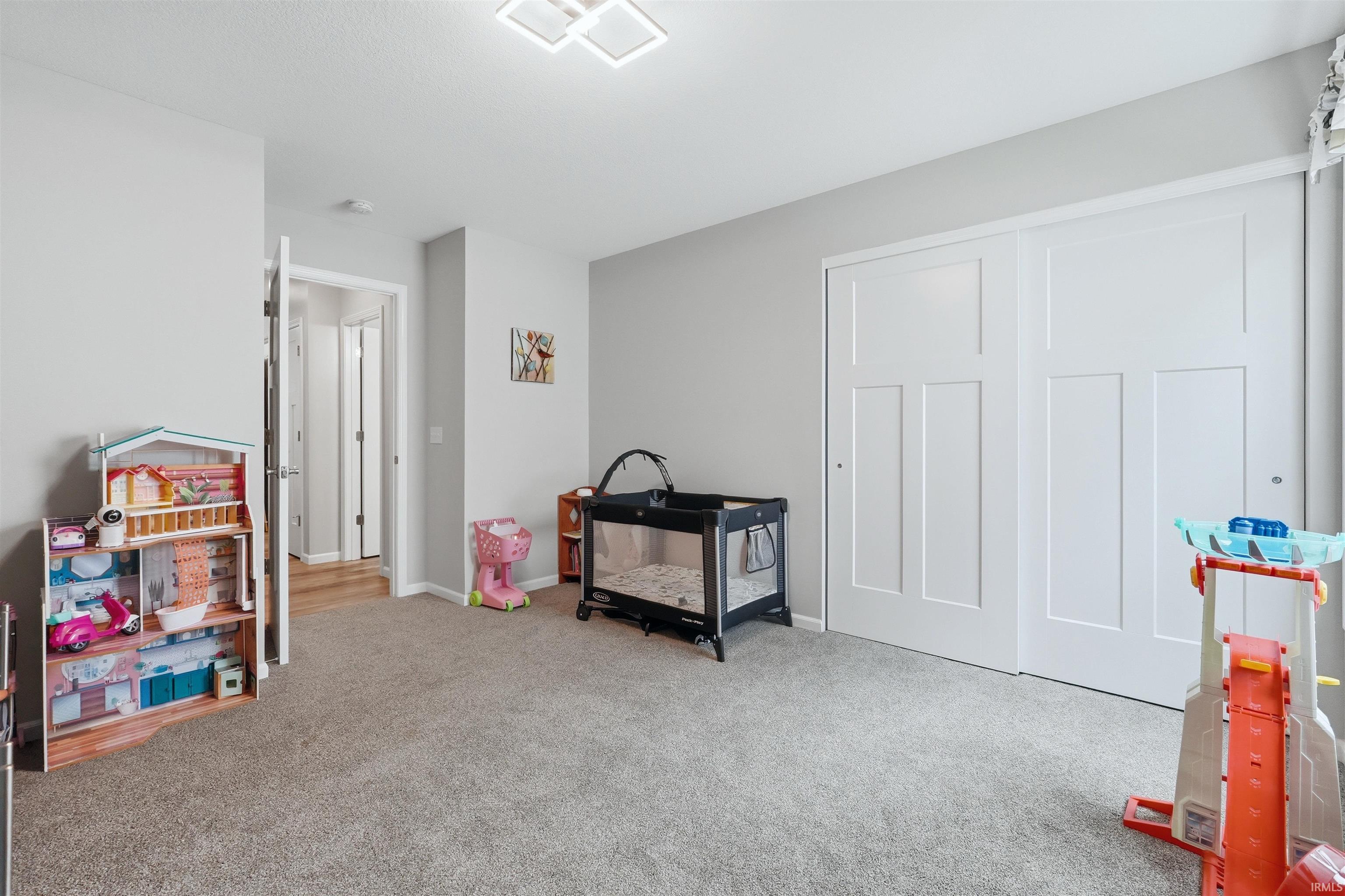 Neutral-toned room with plush carpeting, featuring a modern ceiling light fixture, white interior doors, and a full-height closet with paneled sliding doors