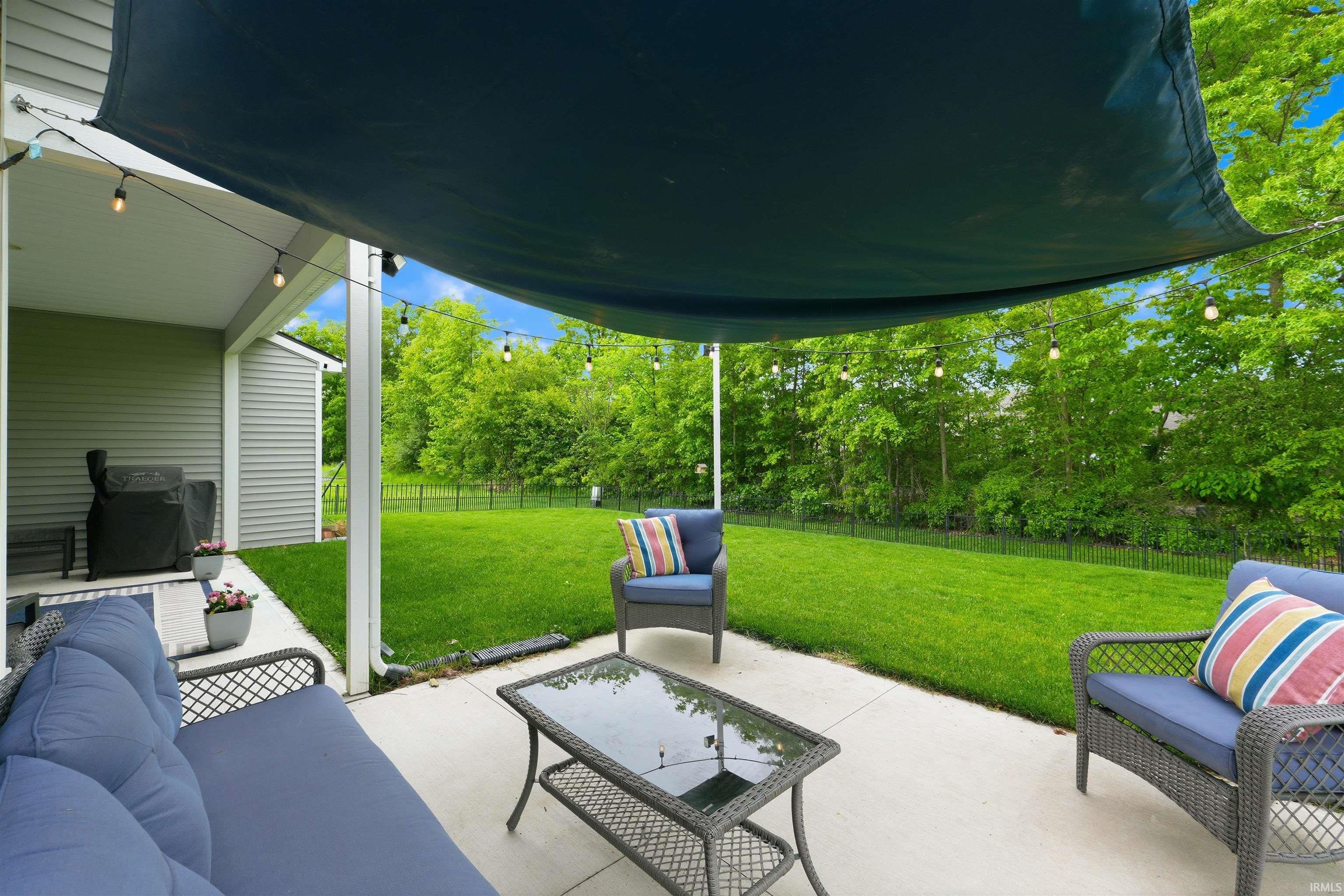Concrete patio with string lighting and a dark fabric shade structure