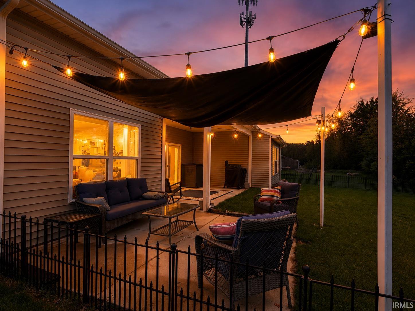 Concrete patio featuring string lighting, a black shade sail, and a black metal fence