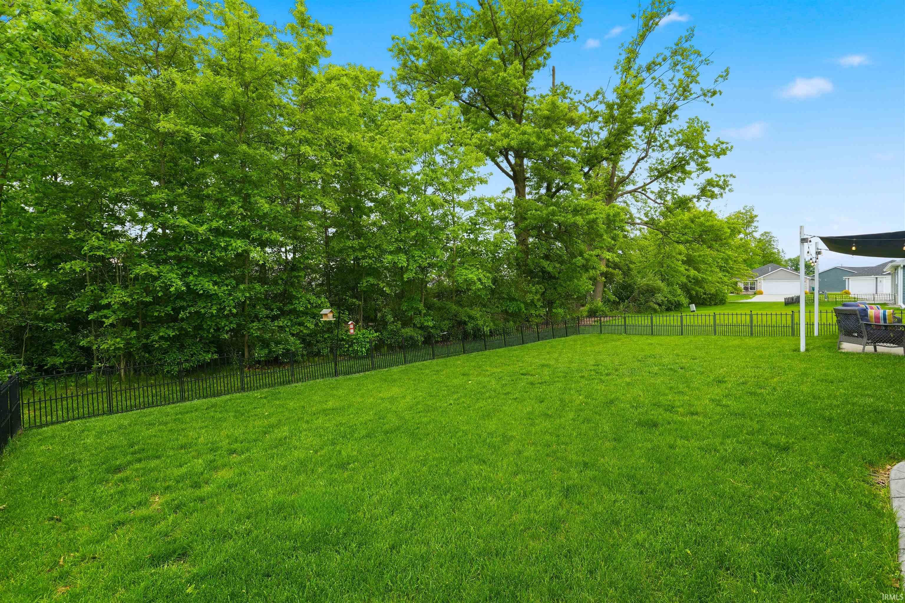 Expansive green lawn bordered by a black metal fence and mature trees