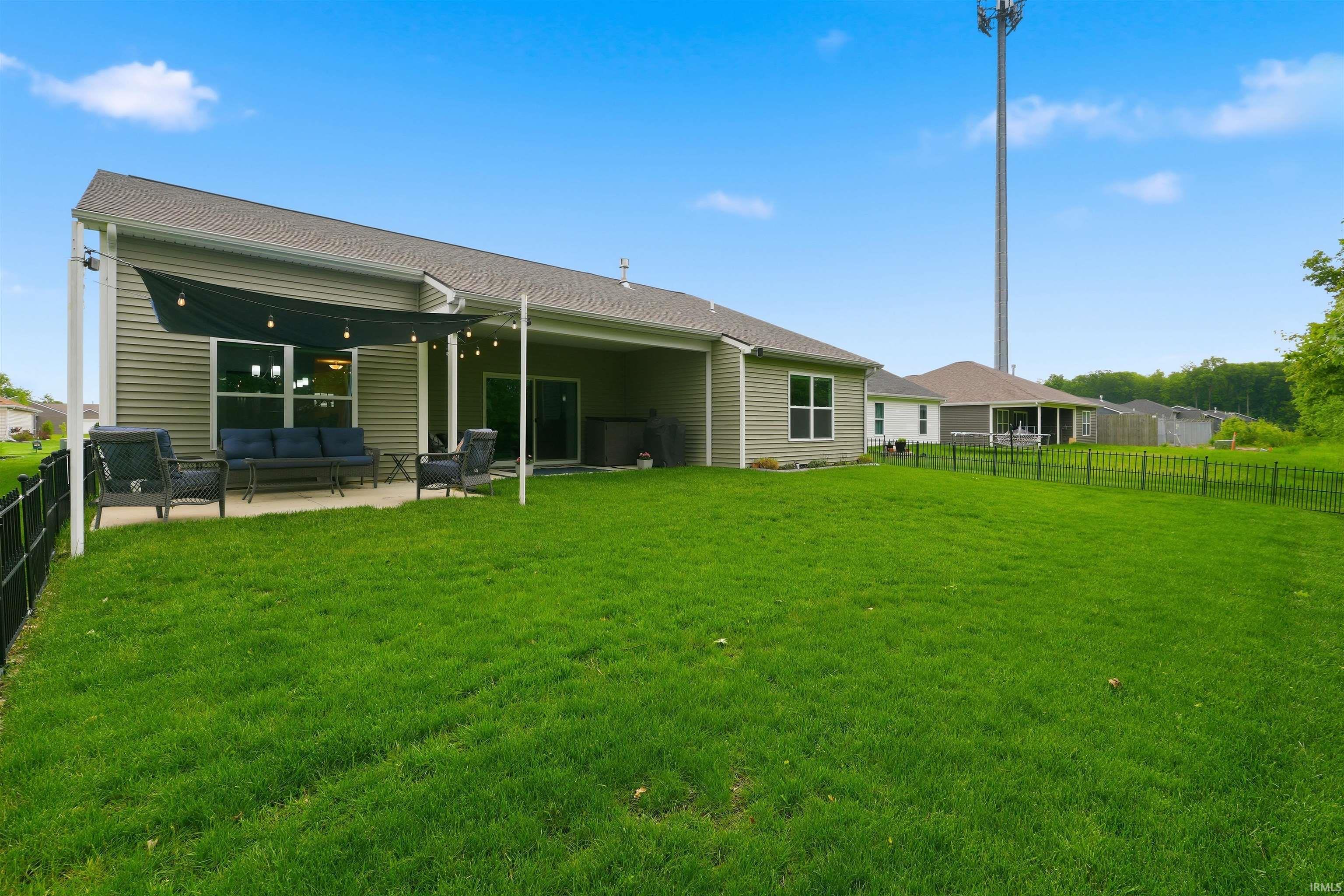 Spacious backyard featuring a covered patio with string lighting, a large concrete slab, and a black metal fence