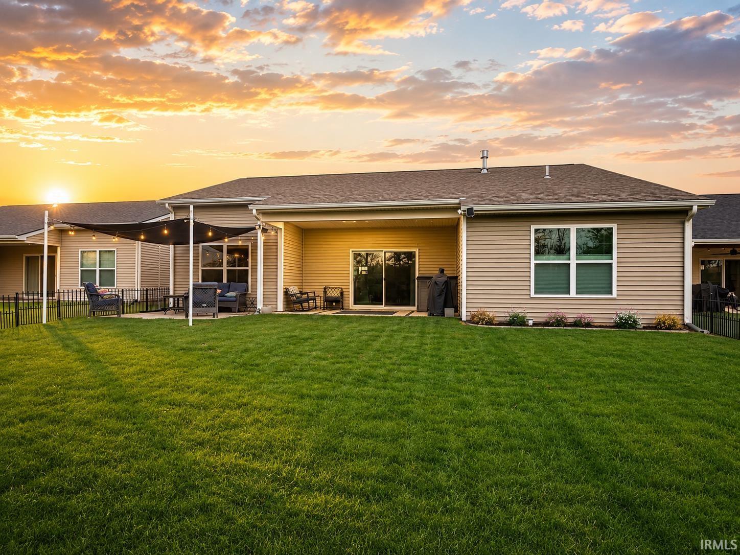 Spacious backyard featuring a manicured lawn, a covered patio area with string lighting, and sliding glass doors