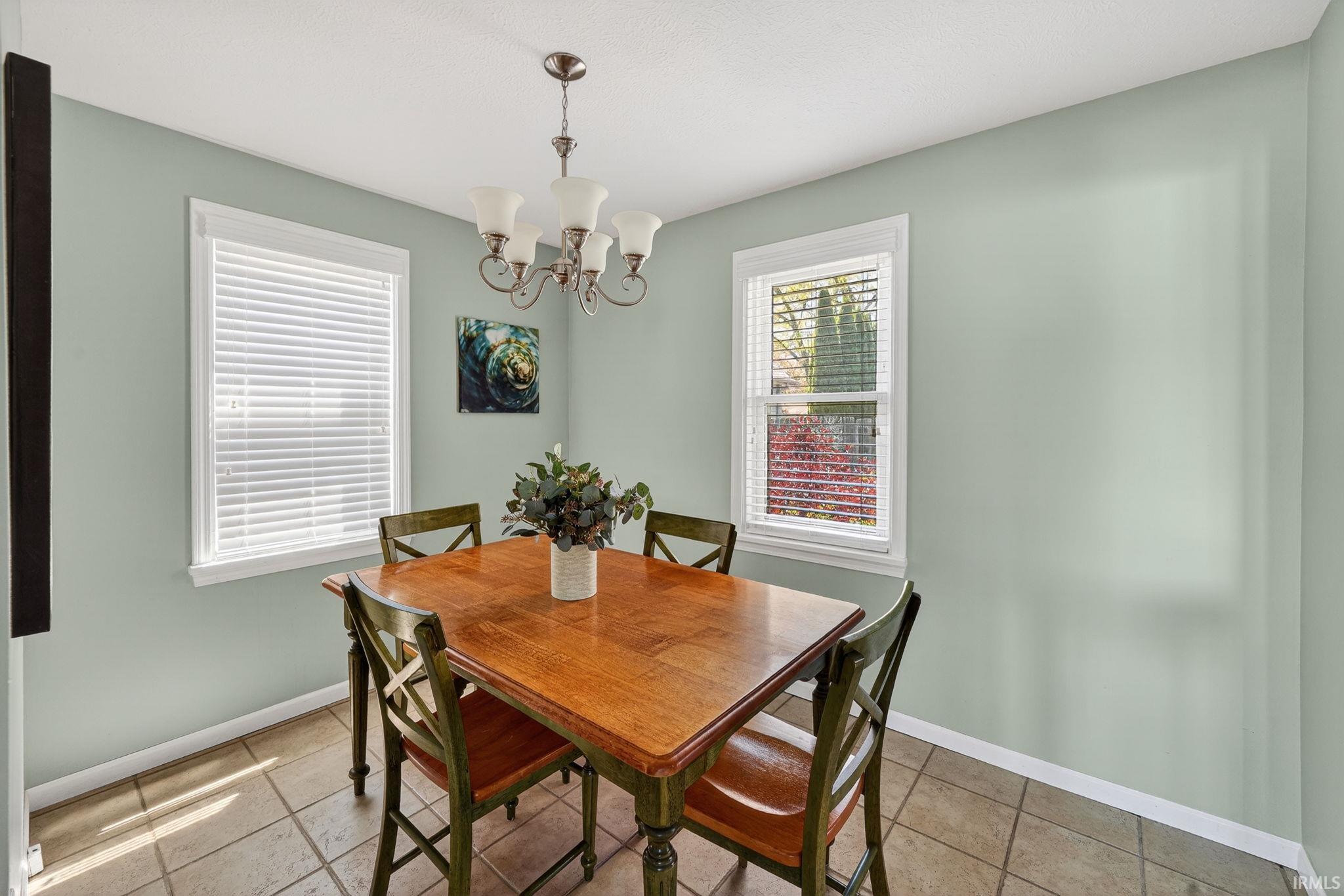 Dining area featuring two windows with white blinds, a bronze-finish chandelier, and neutral tile flooring