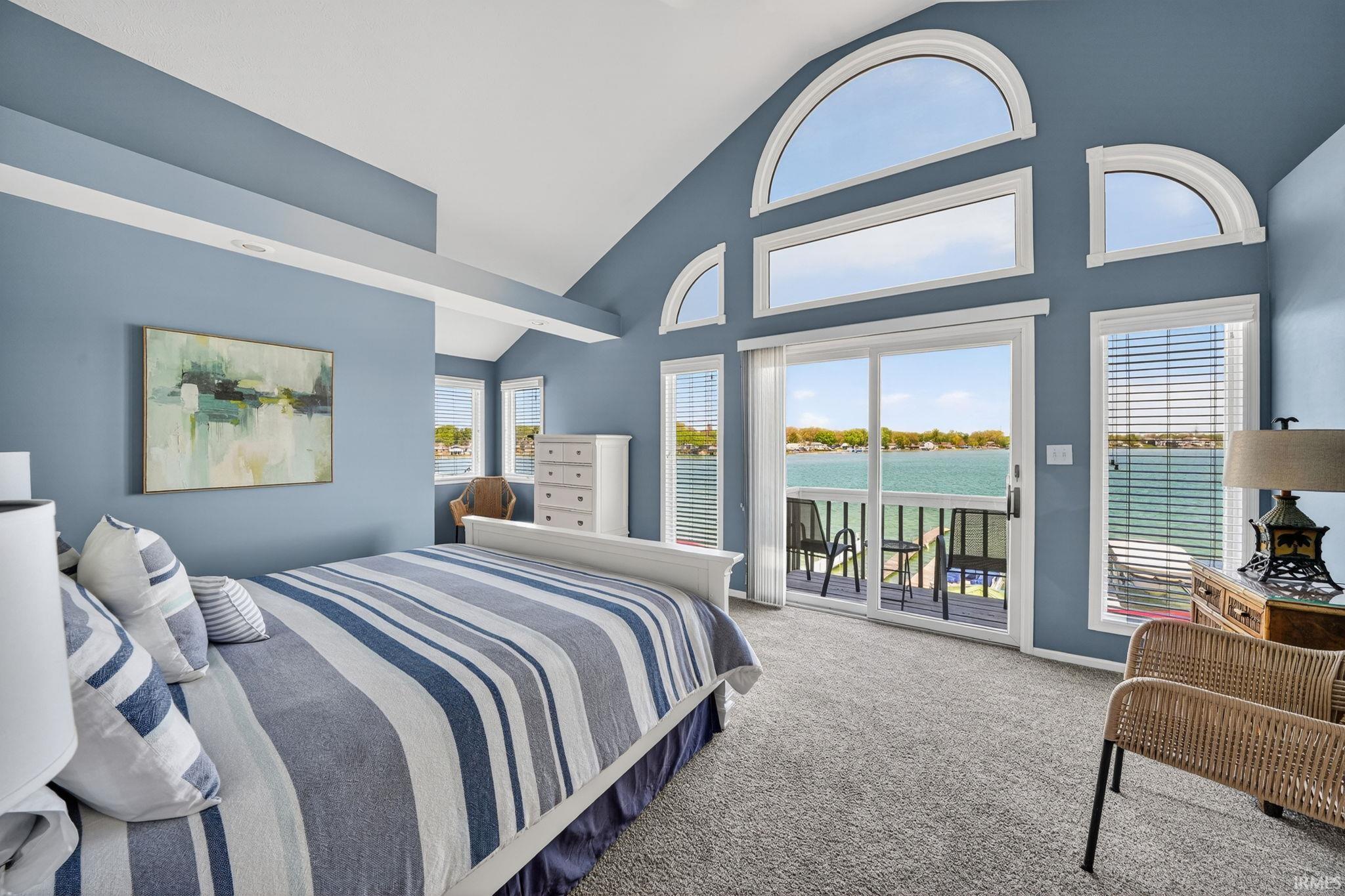 Spacious room featuring vaulted ceilings, a large sliding glass door opening to a balcony, and multiple arched transom windows