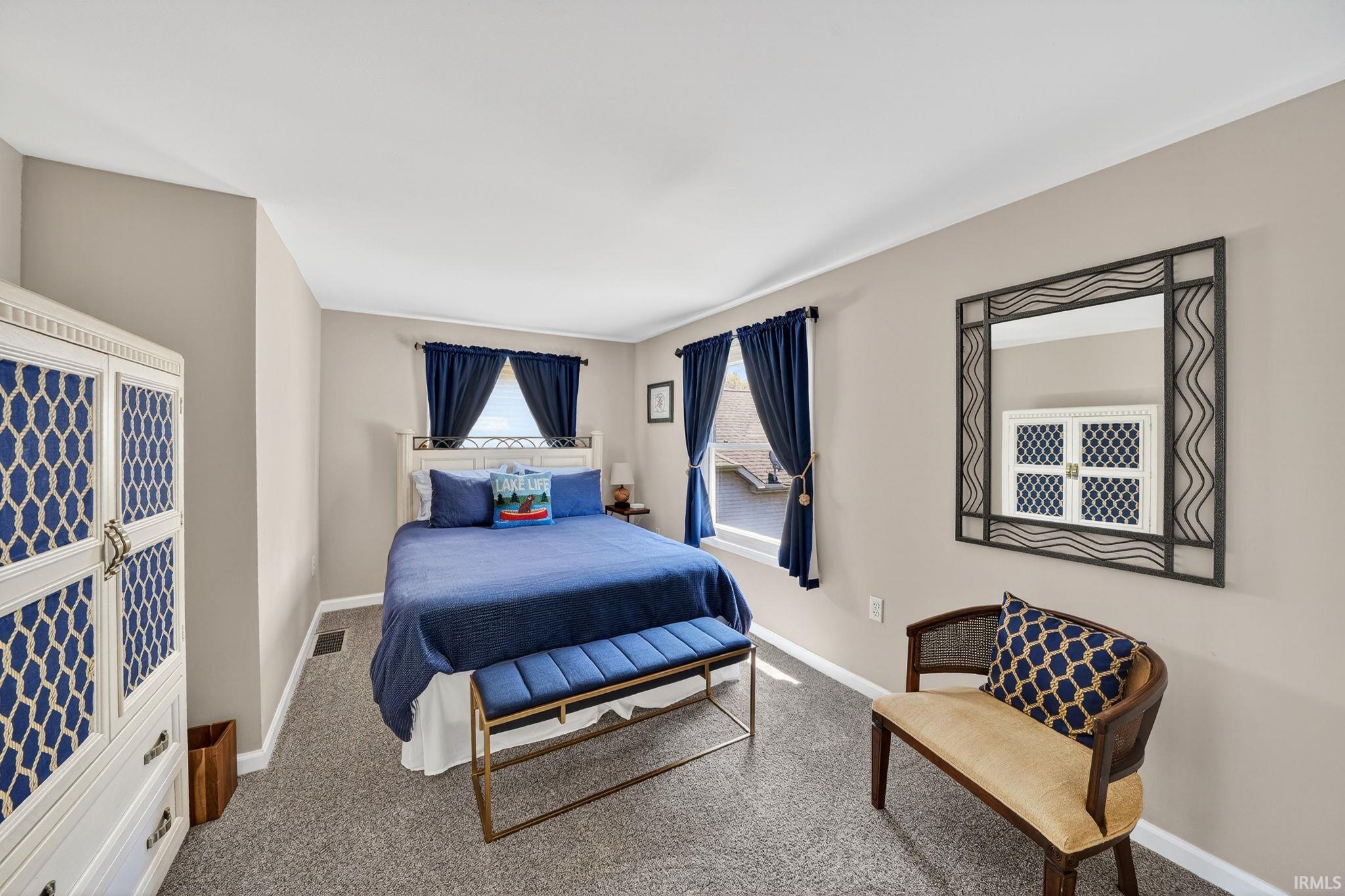 Neutral tone wall paint, carpet flooring, baseboard trim, and two windows with natural light