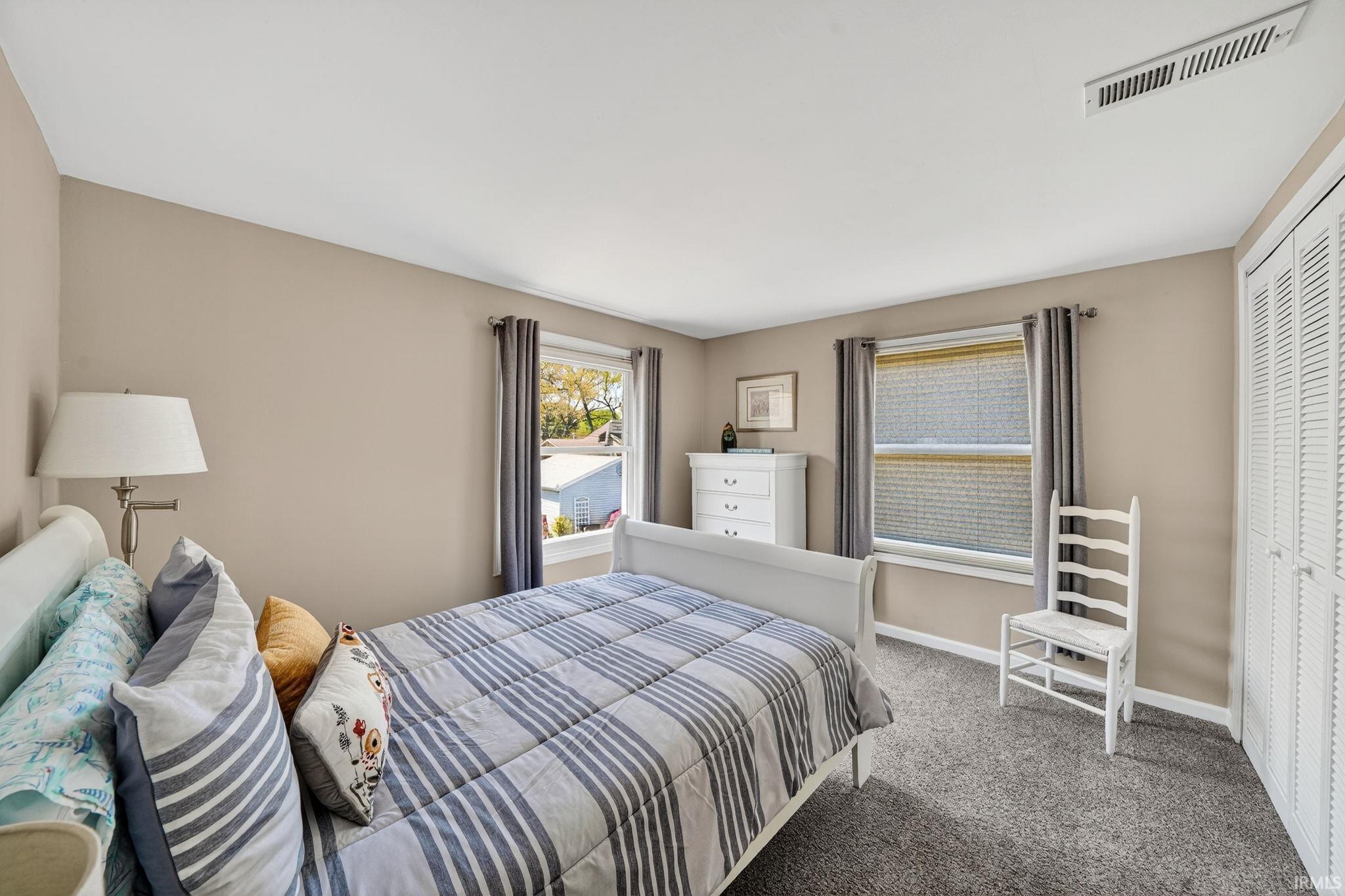 Bedroom featuring two windows with neutral drapes, textured grey carpeting, a white ceiling, and light beige wall finishes