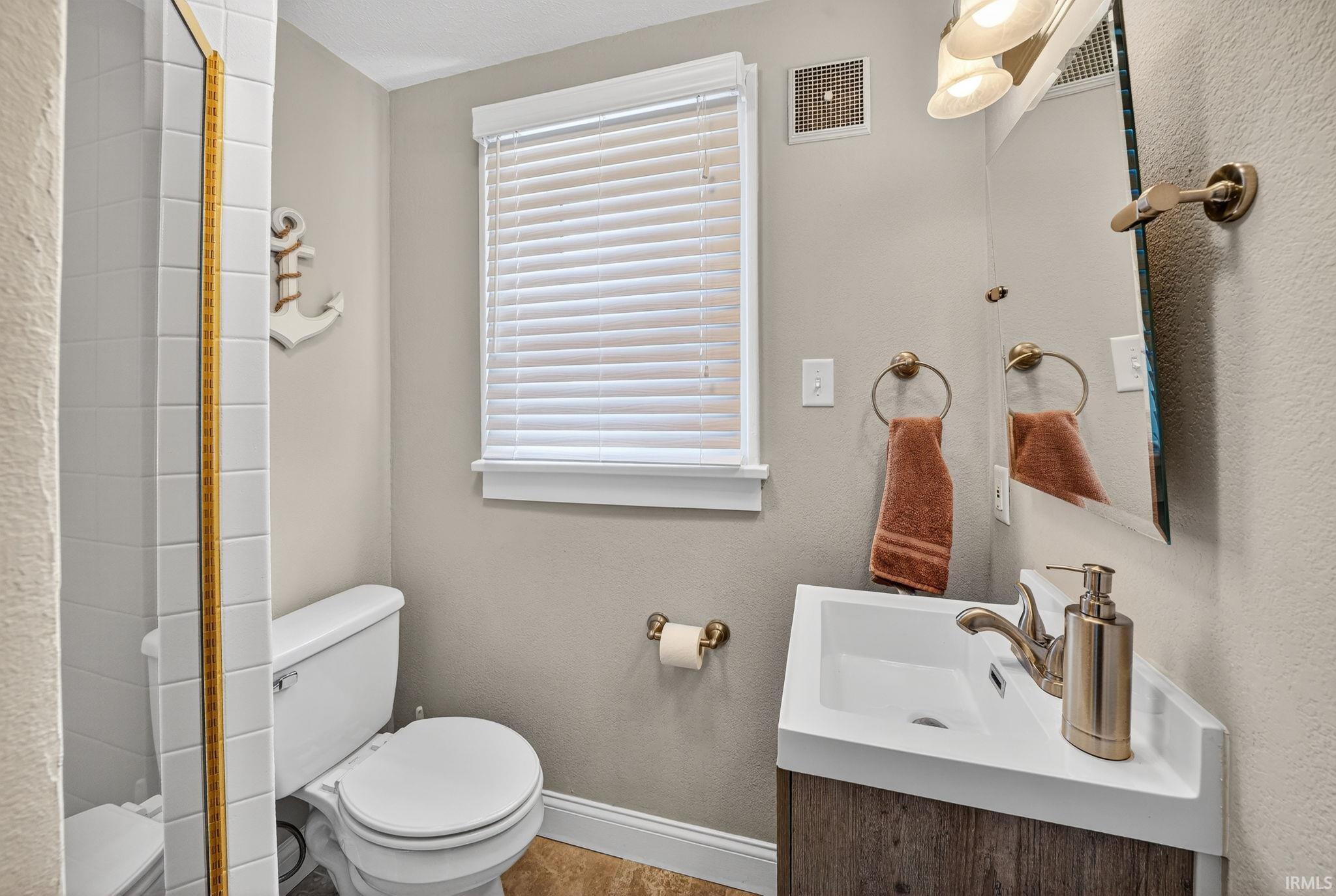 Bathroom featuring a corner vanity with integrated sink, wood-finish cabinetry, and brushed brass fixtures