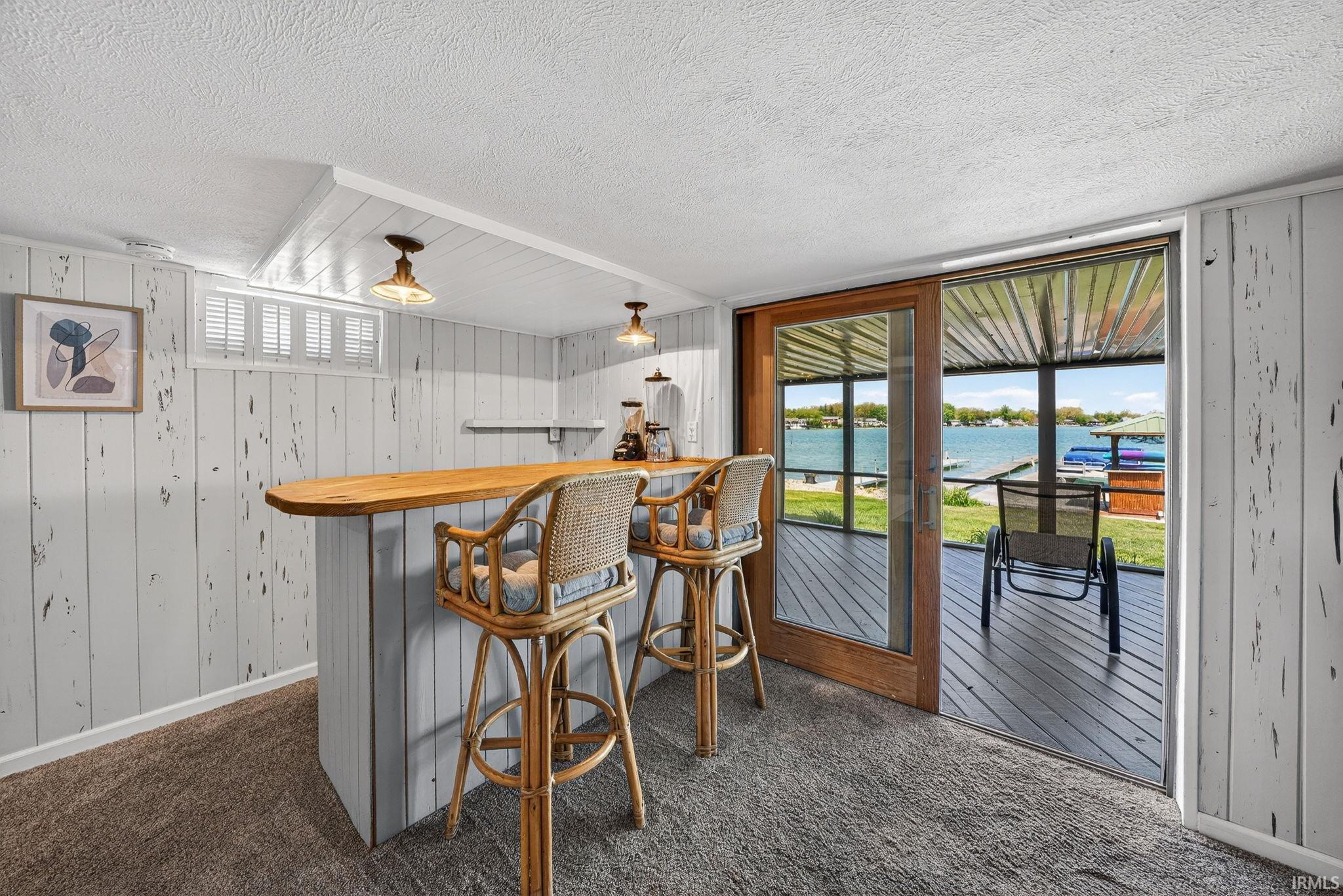 Recreational room featuring a built-in bar with a natural wood countertop, textured wall paneling, and a full glass sliding door opening to an outdoor deck