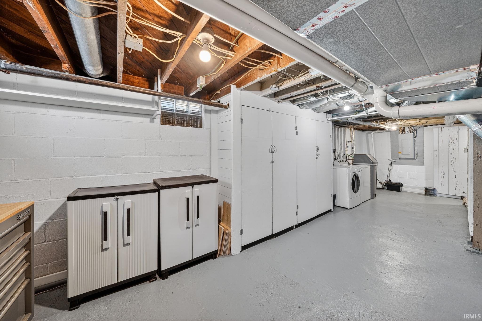 Basement area featuring painted concrete block walls, exposed wood ceiling joists, and a painted concrete floor