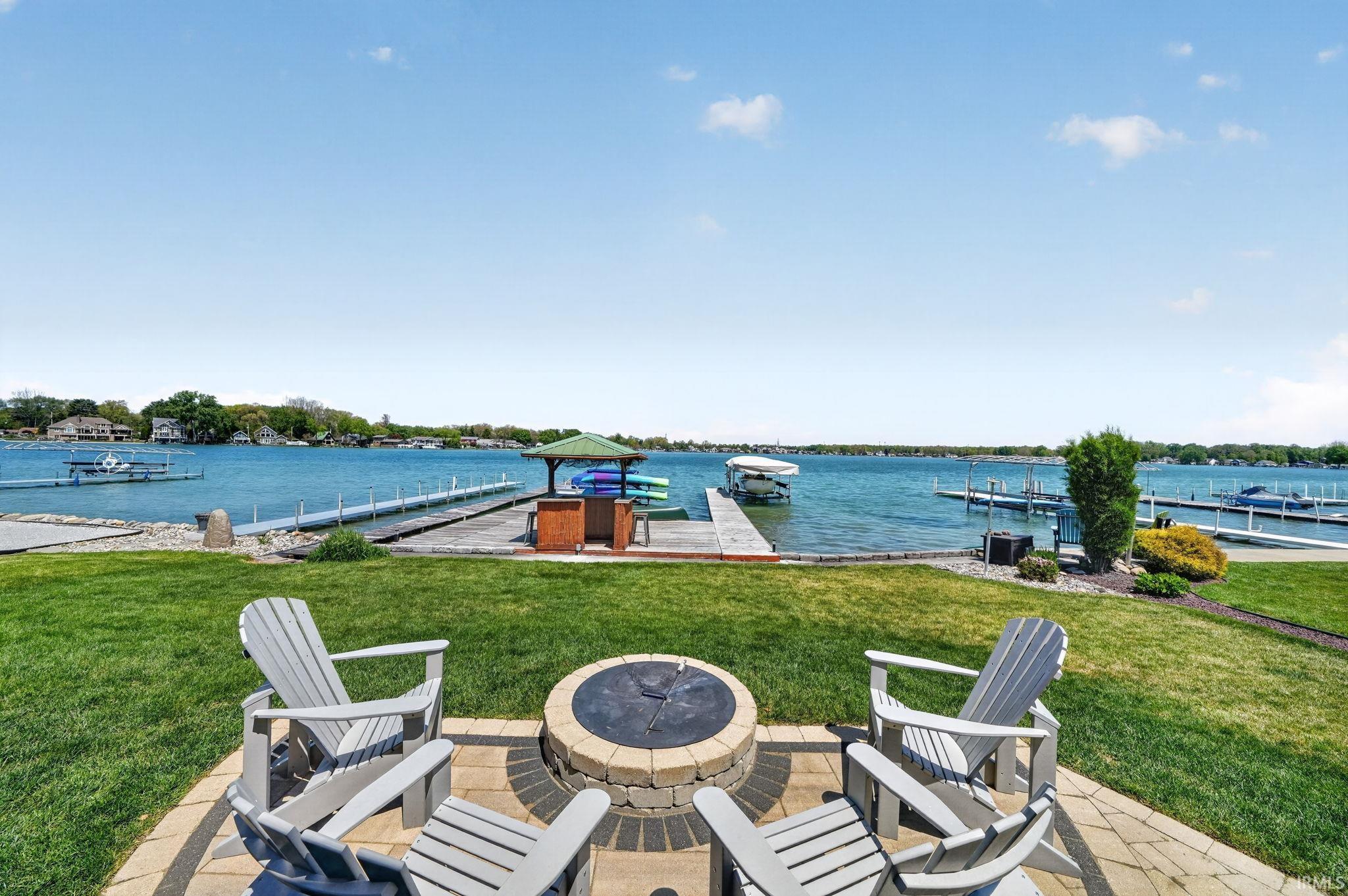 Waterside patio featuring a paver-stone fire pit, manicured lawn, and multiple boat docks
