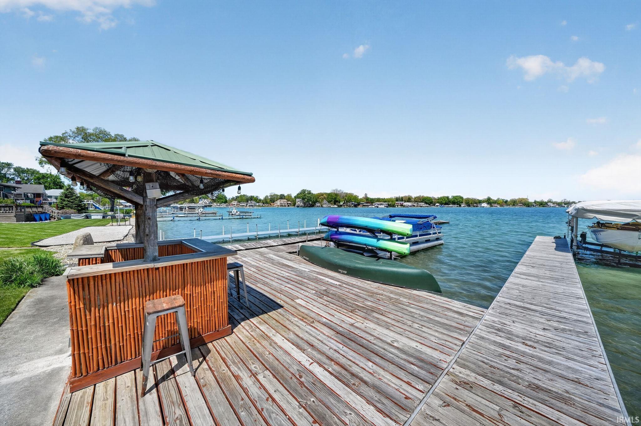 Private dock featuring a built-in tiki bar with a green metal roof, extensive wooden decking, and direct water access