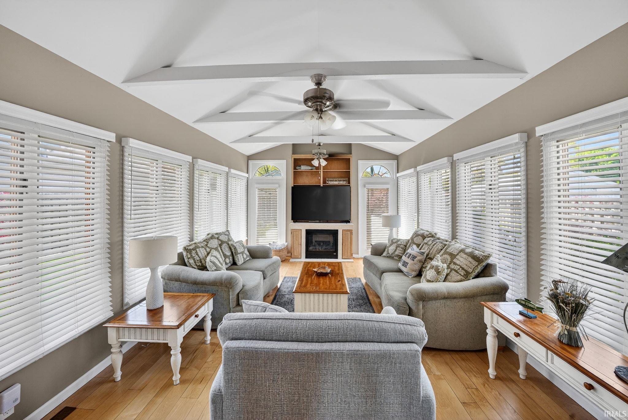 Sunroom featuring vaulted ceilings with exposed beams, wood-finish flooring, and multiple large windows with horizontal blinds