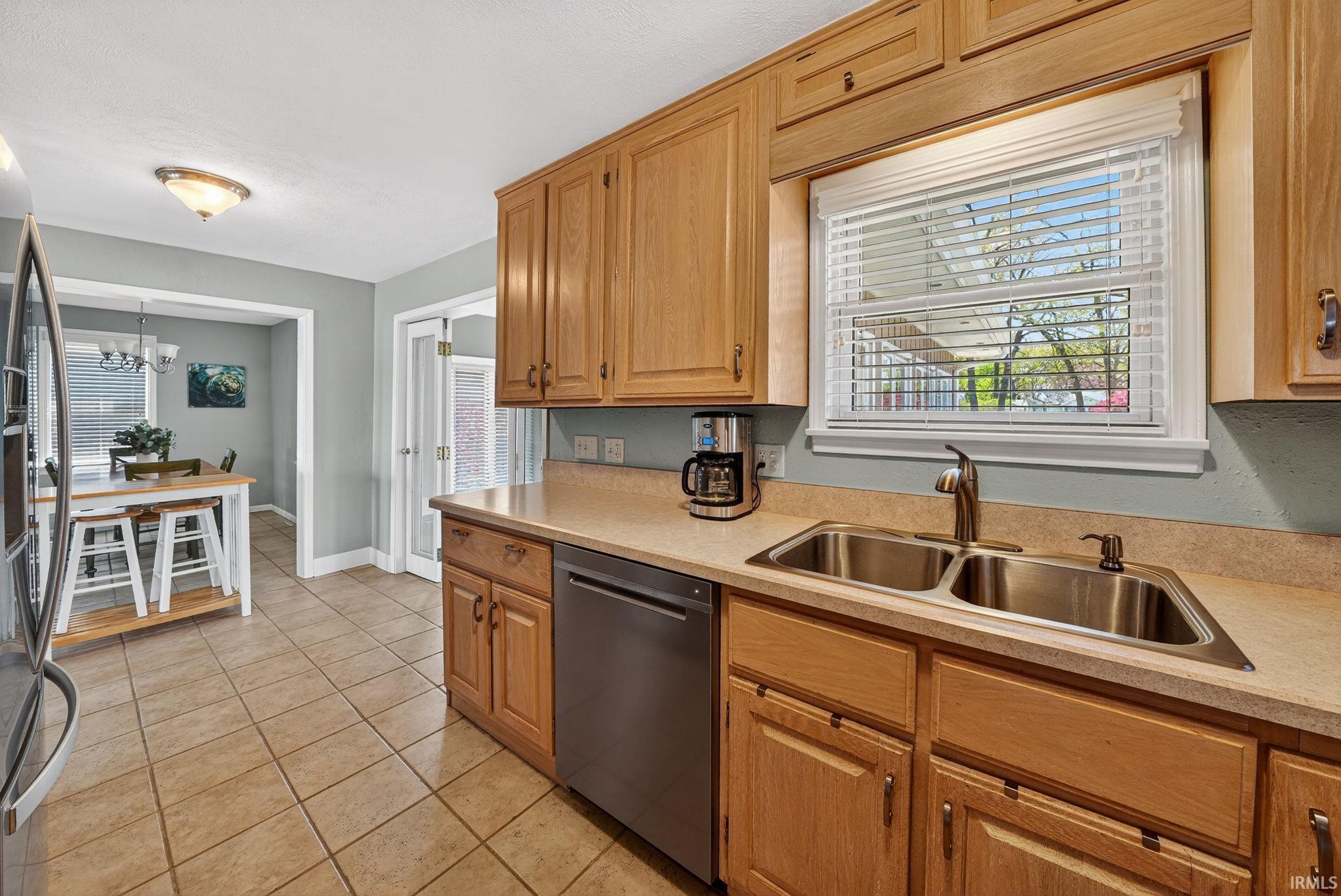 Kitchen featuring wood cabinetry, stainless steel double basin sink with brushed nickel faucet, and a window with white blinds