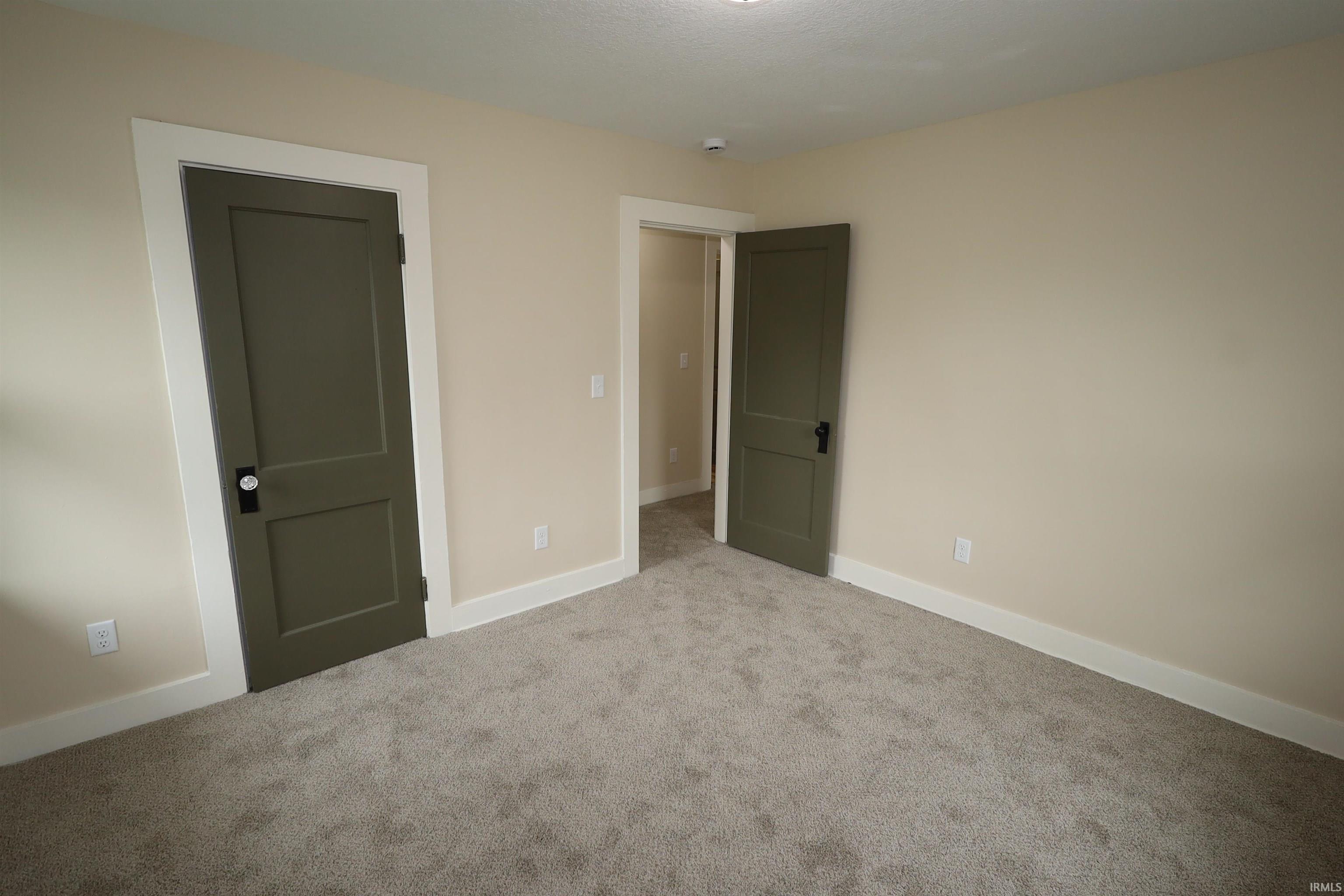 Interior room featuring neutral wall paint, gray carpet flooring, white baseboards, and a paneled interior door with dark hardware