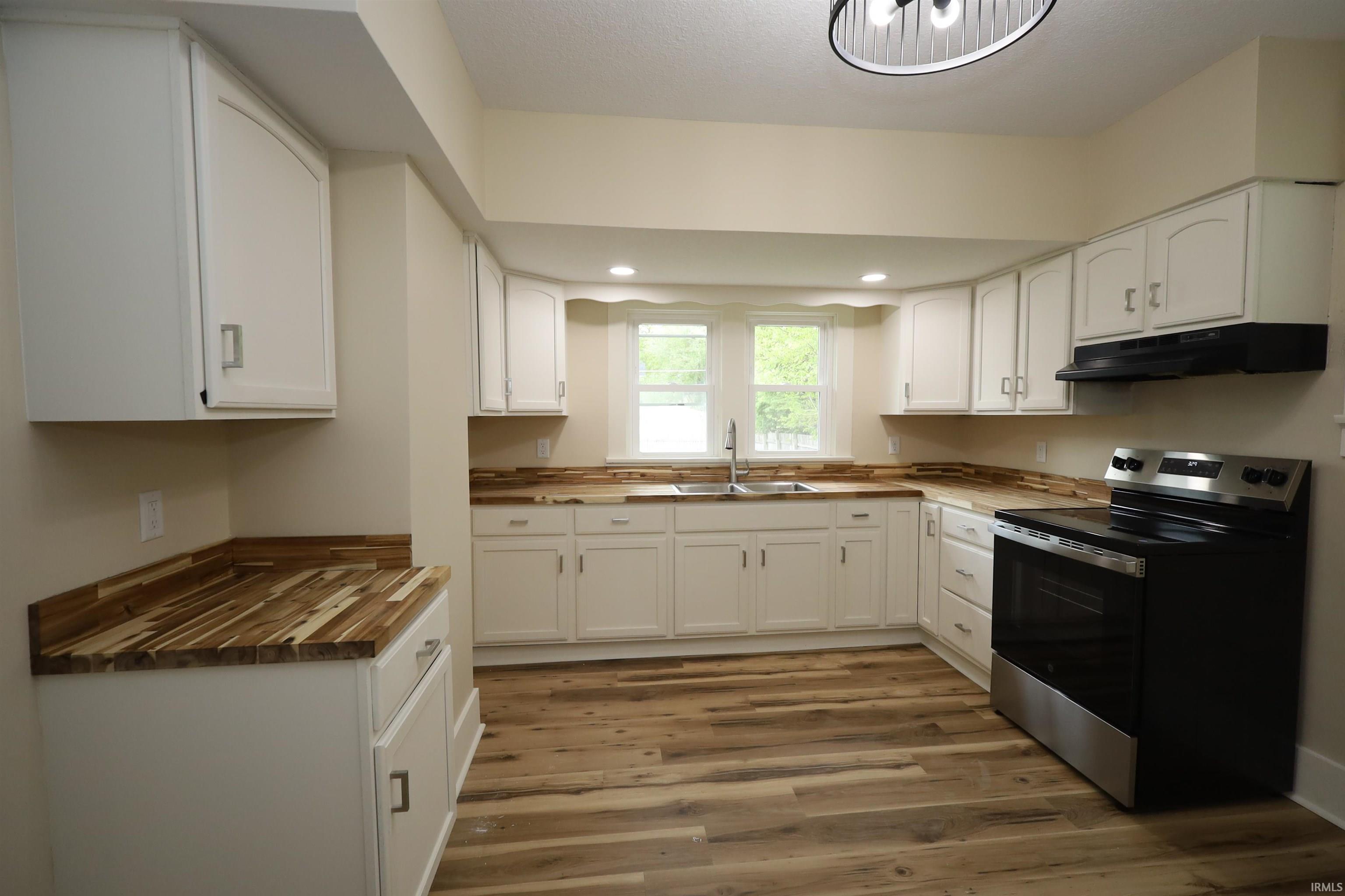 Kitchen featuring white cabinetry, wood-finish countertops, stainless steel sink, wood-finish flooring, and a stainless steel oven range