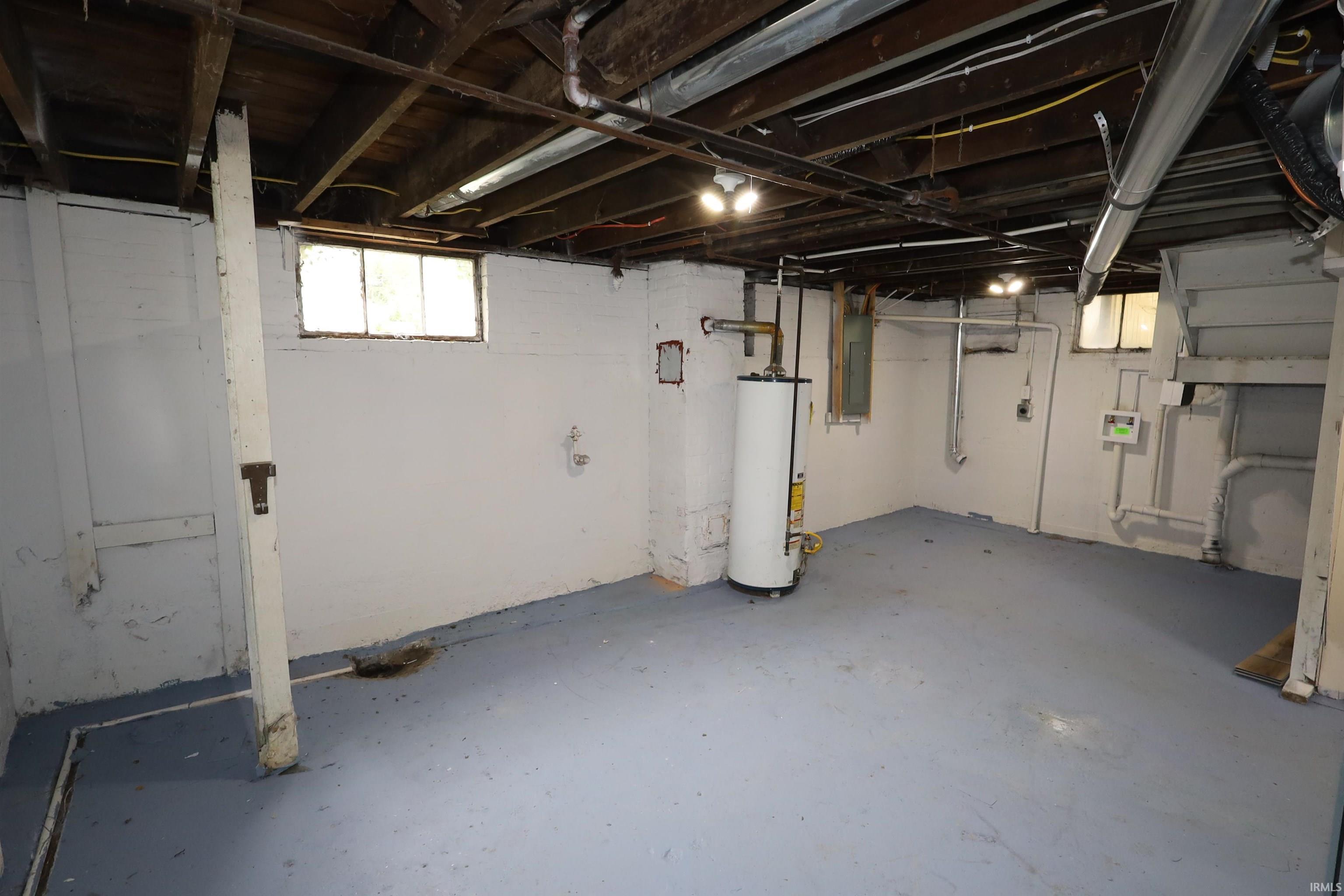 Expansive lower level featuring painted concrete floors, exposed ceiling joists, and multiple utility access points