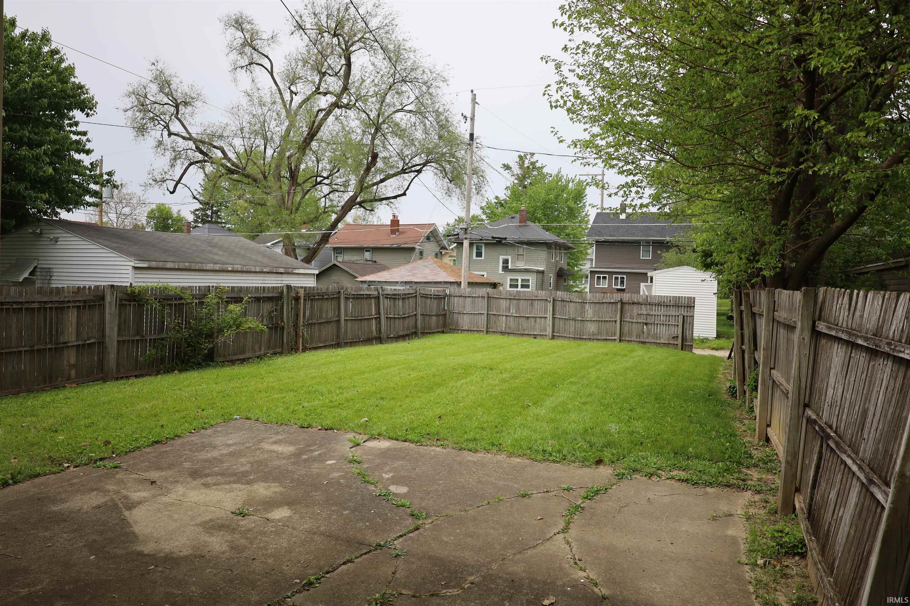 Spacious fenced backyard featuring a concrete patio and mature perimeter trees