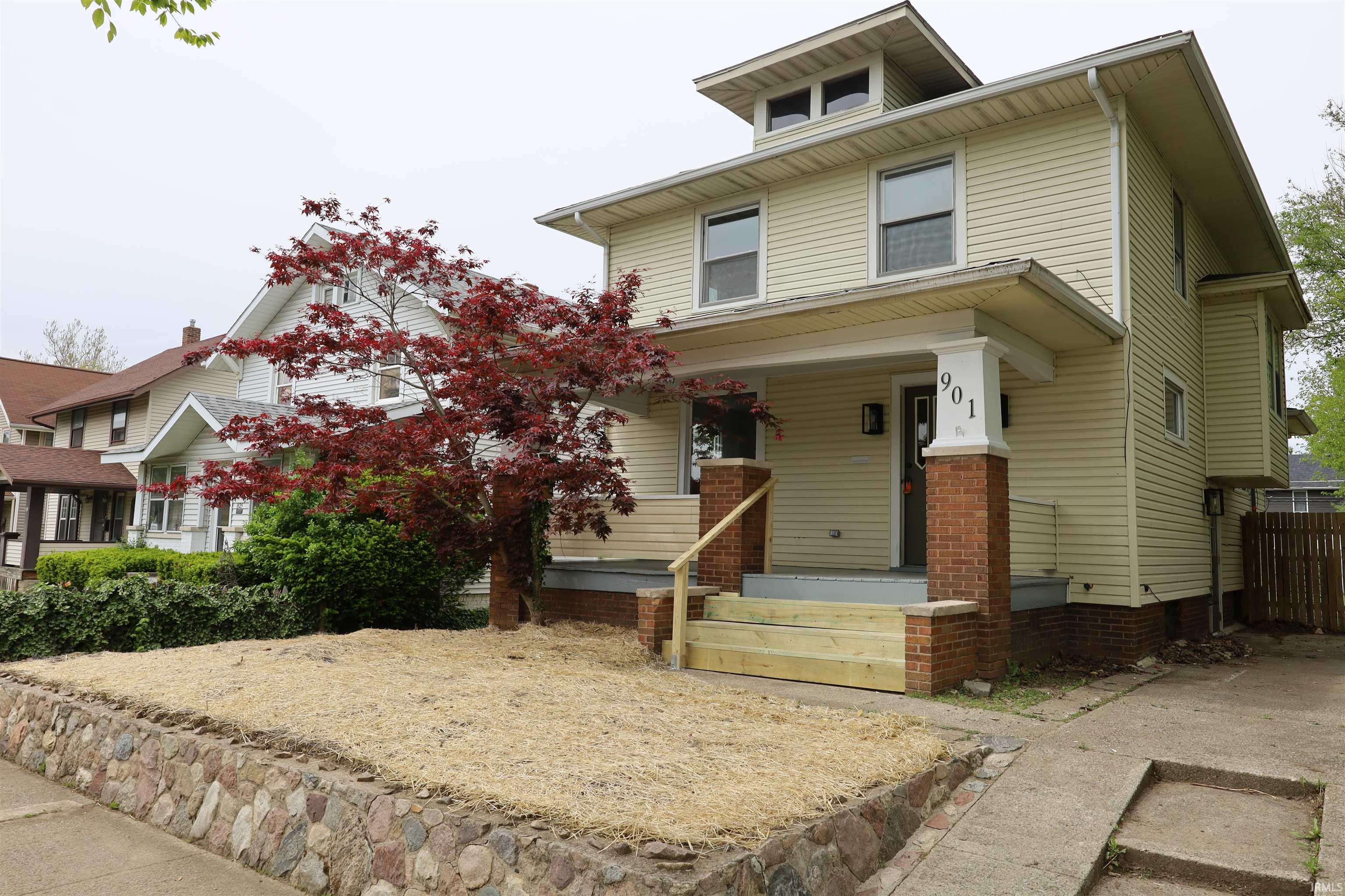 Cream-toned siding residence featuring a prominent front porch with brick pillars and new wood stairs
