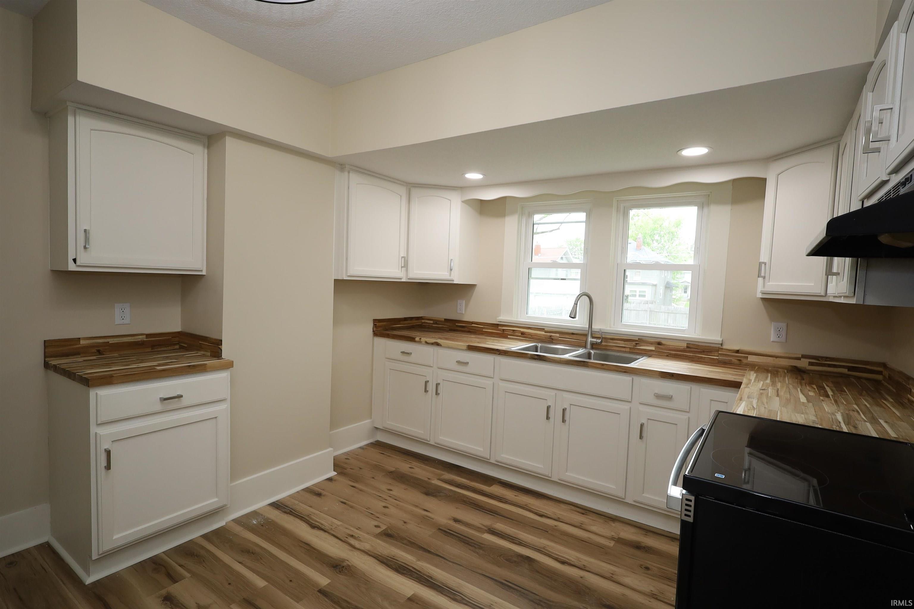 Kitchen featuring white cabinetry, wood-finish countertops, stainless steel double basin sink with gooseneck faucet, recessed lighting, and wood-finish flooring
