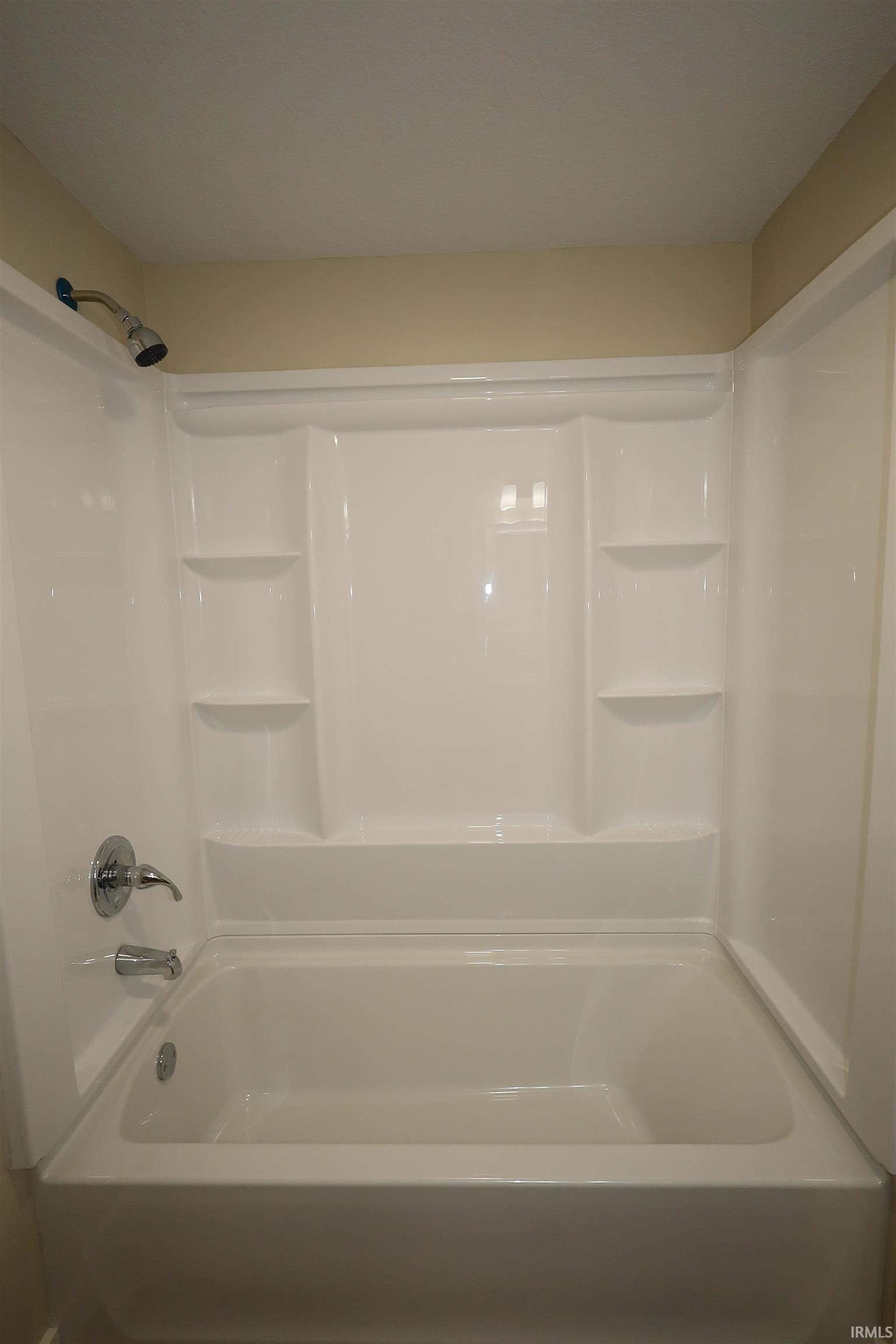 White bathtub and shower combination unit featuring an integrated soap dish and shelving
