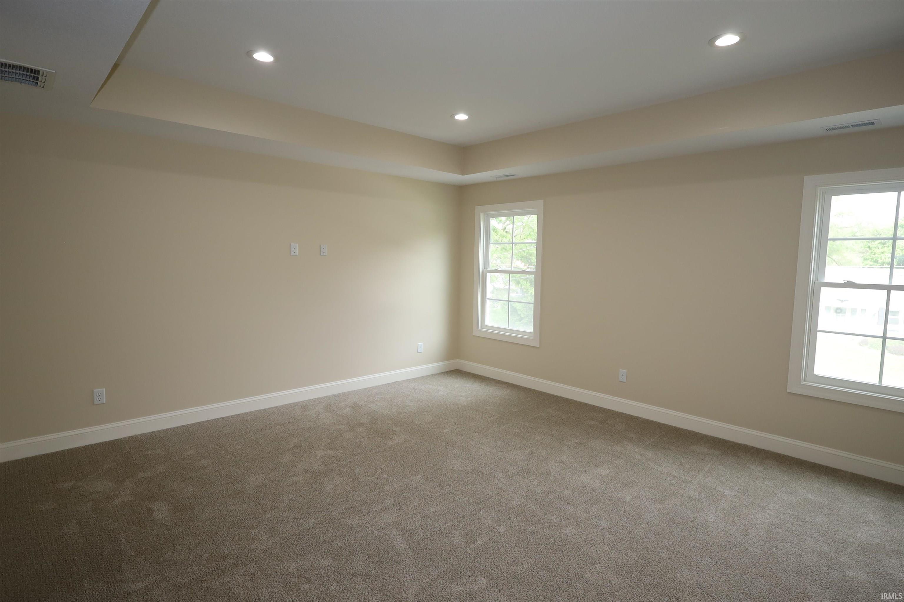 Spacious room featuring a tray ceiling with recessed lighting, two double-hung windows, and neutral carpeting