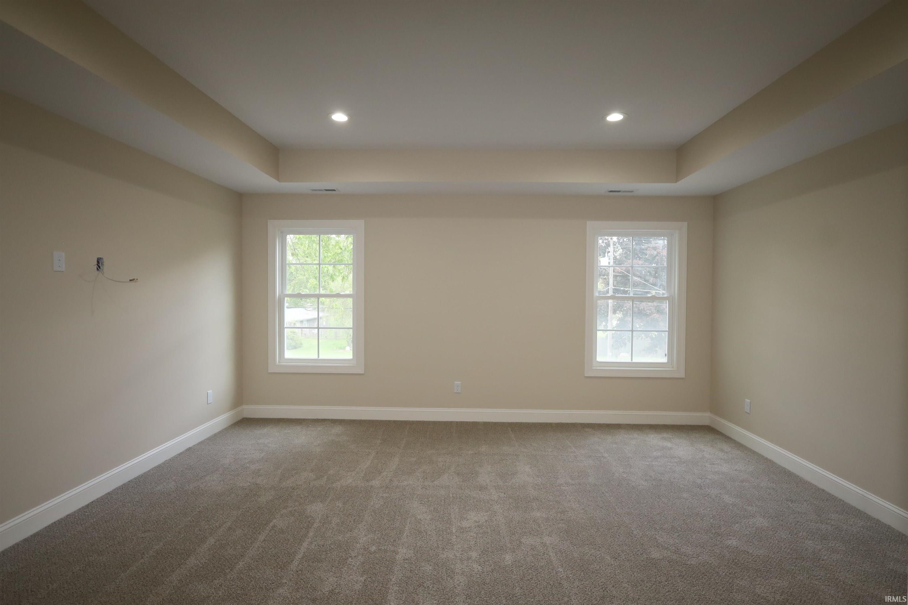 Spacious room featuring neutral carpeting, light-toned walls, and a tray ceiling with recessed lighting