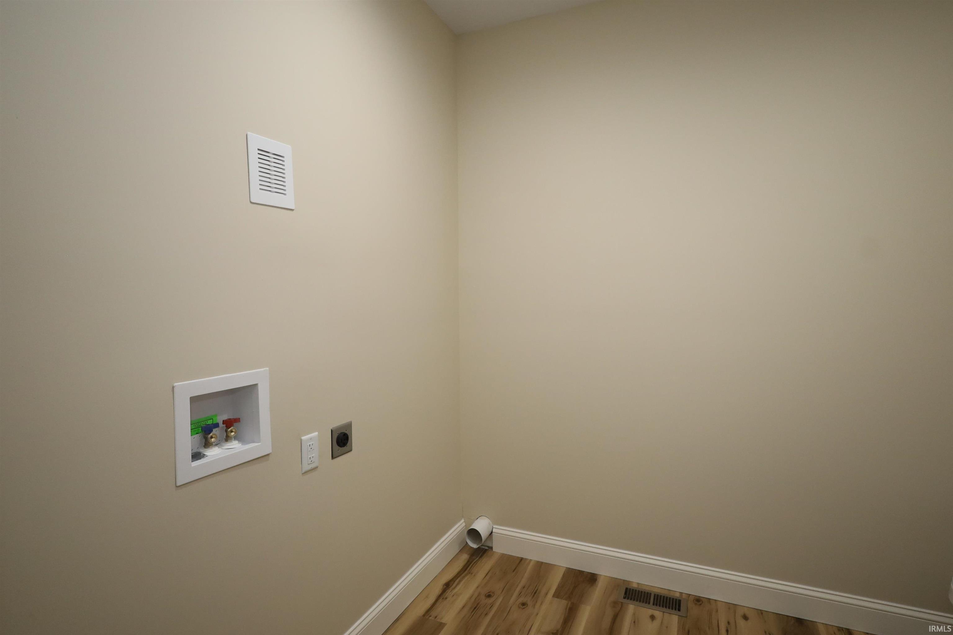 Laundry utility area featuring a wall-mounted hookup box, dryer vent, and wood-finish flooring with white baseboards