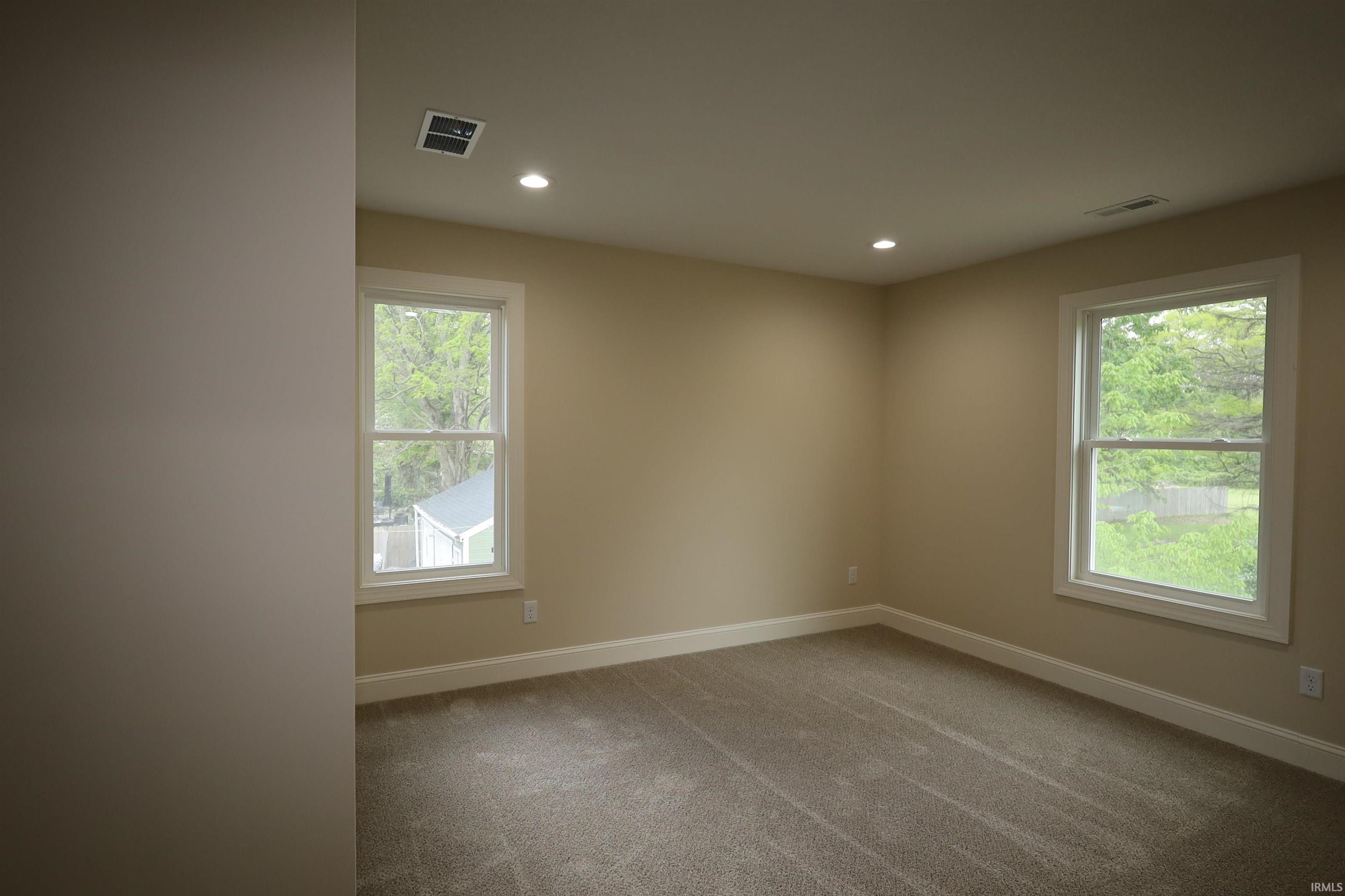 Neutral-toned room featuring two double-hung windows with white trim, recessed lighting, and a beige carpeted floor
