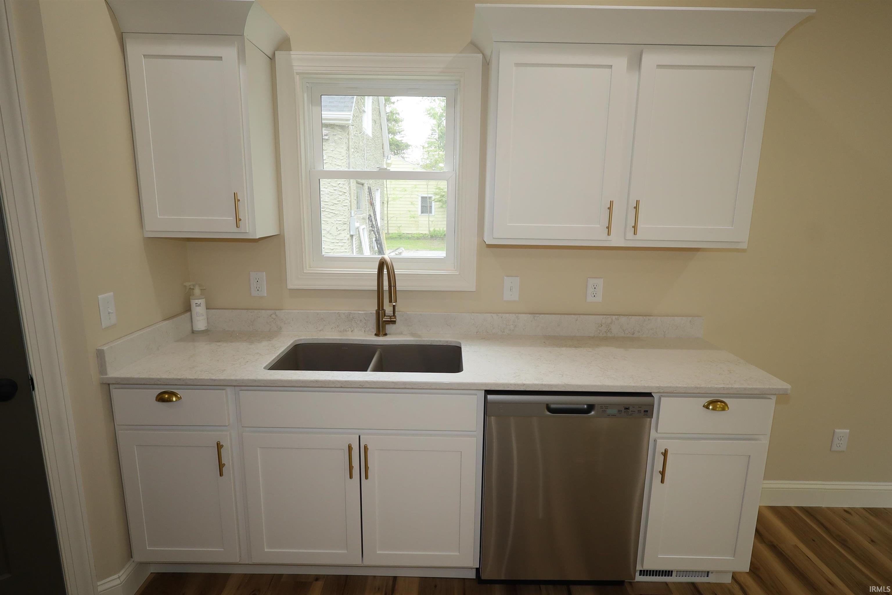 White shaker-style cabinetry with gold-tone hardware, a double basin stainless steel sink, and a brushed gold-tone faucet