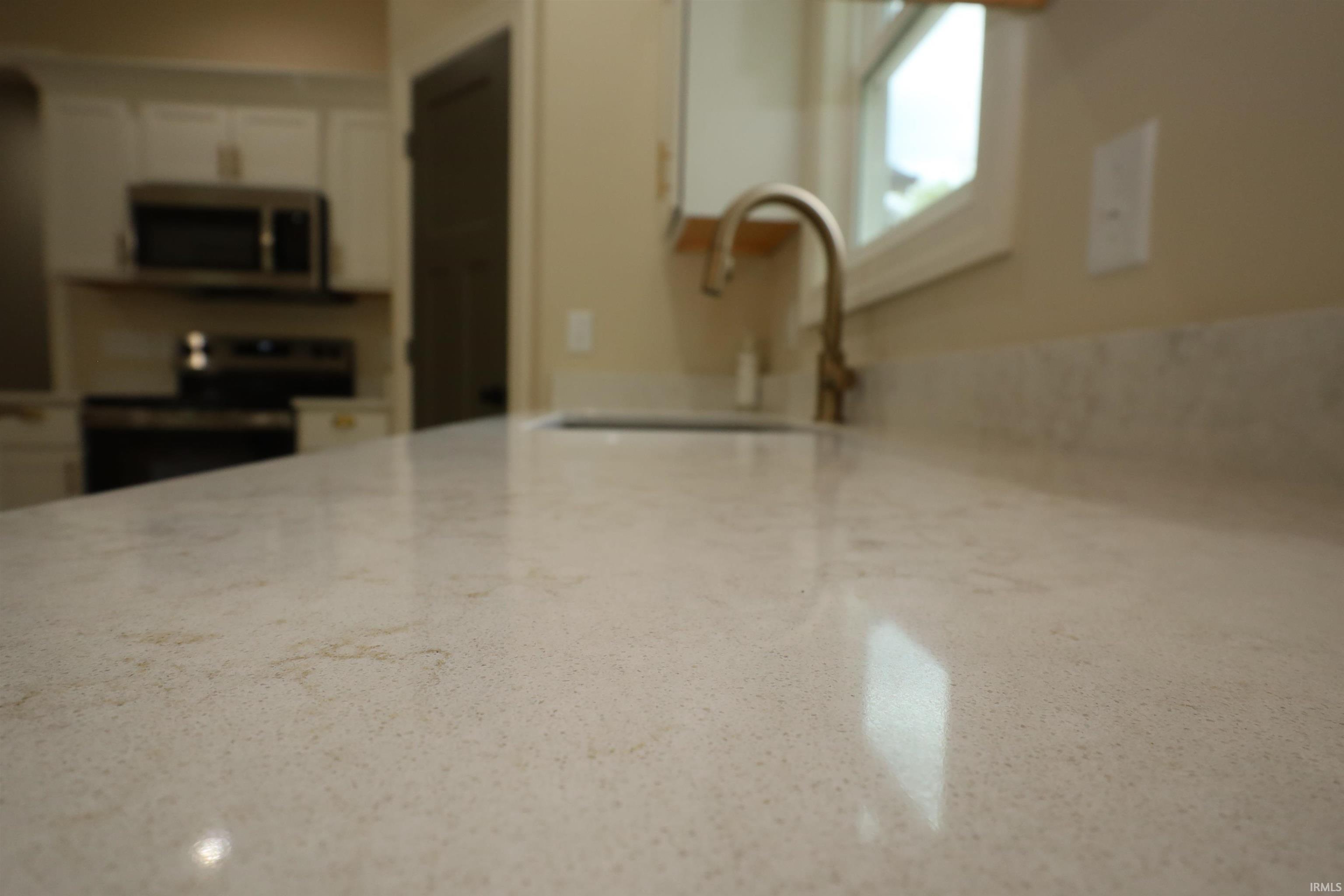 Kitchen featuring light-toned countertops, a stainless steel sink with a high-arch faucet, and white cabinetry