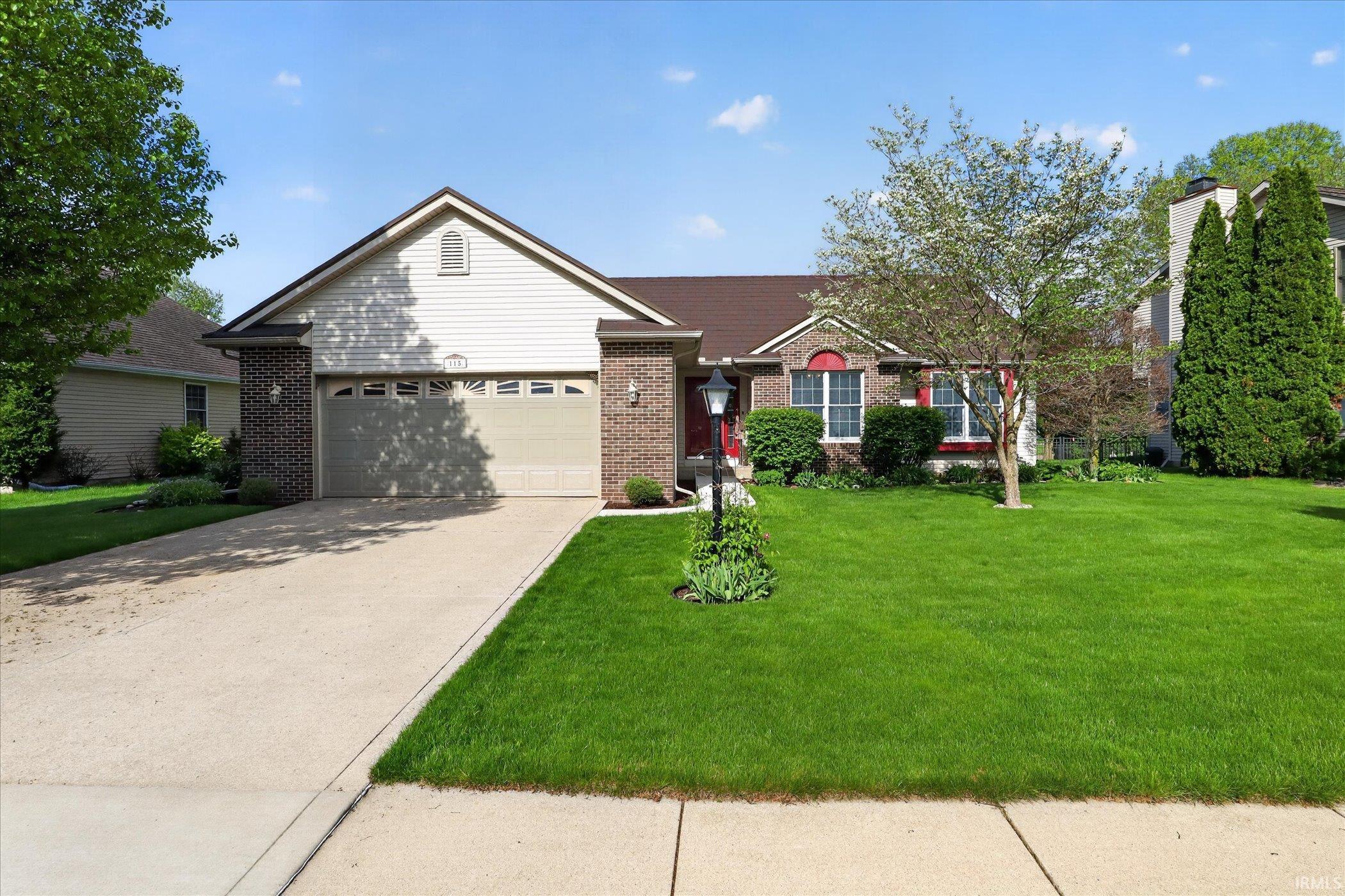 Ranch-style residence featuring a brick and siding exterior, an attached garage, a concrete driveway, a manicured lawn, and mature landscaping