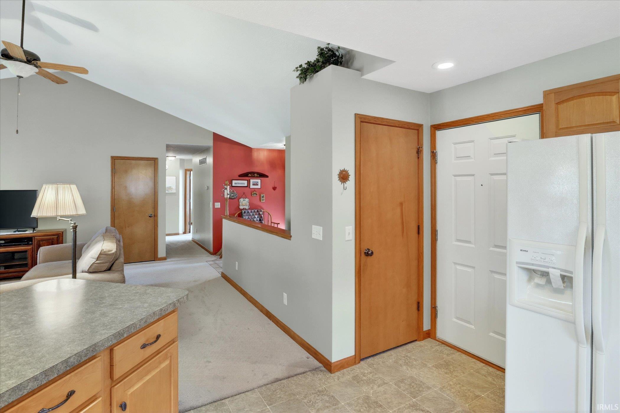 Vaulted ceiling with ceiling fan in the living area, featuring light wood-finish doors and trim, a half-wall partition, and light-toned carpet