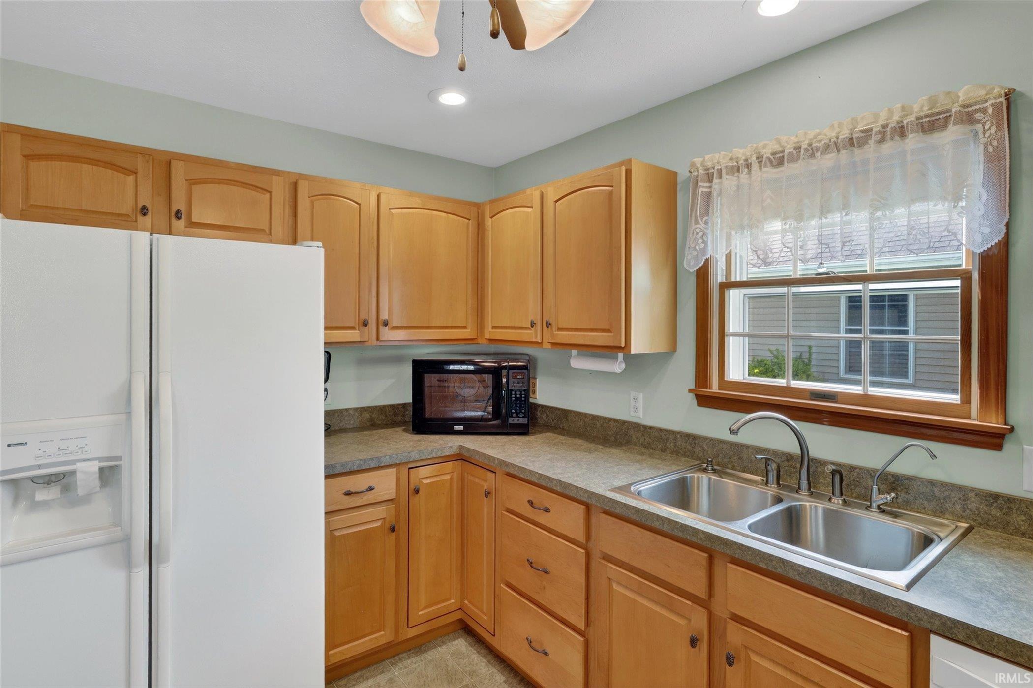 Kitchen featuring natural wood cabinetry, a dual basin stainless steel sink, and light-toned countertops
