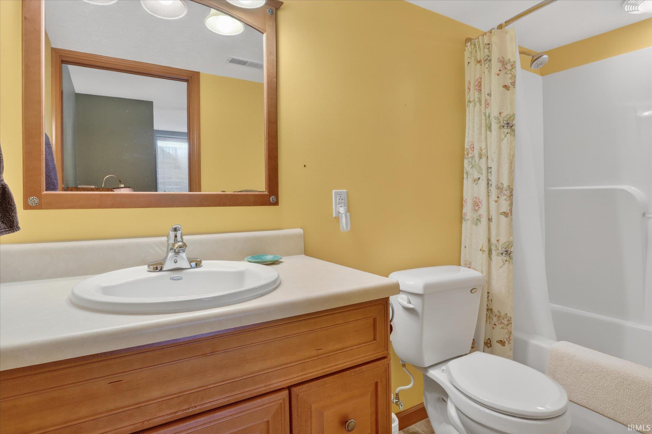 Bathroom featuring a wood-finish vanity with a built-in sink, a framed mirror, and a white toilet
