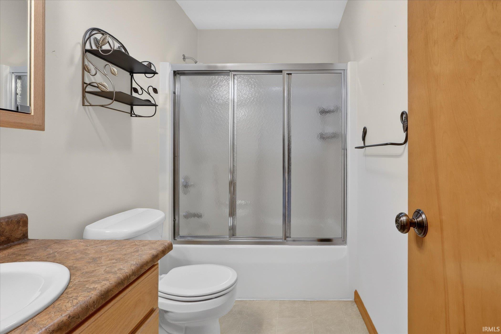 Bathroom featuring a full shower with sliding glass doors, a single vanity with an integrated sink and laminate countertop, a toilet, and a medicine cabinet