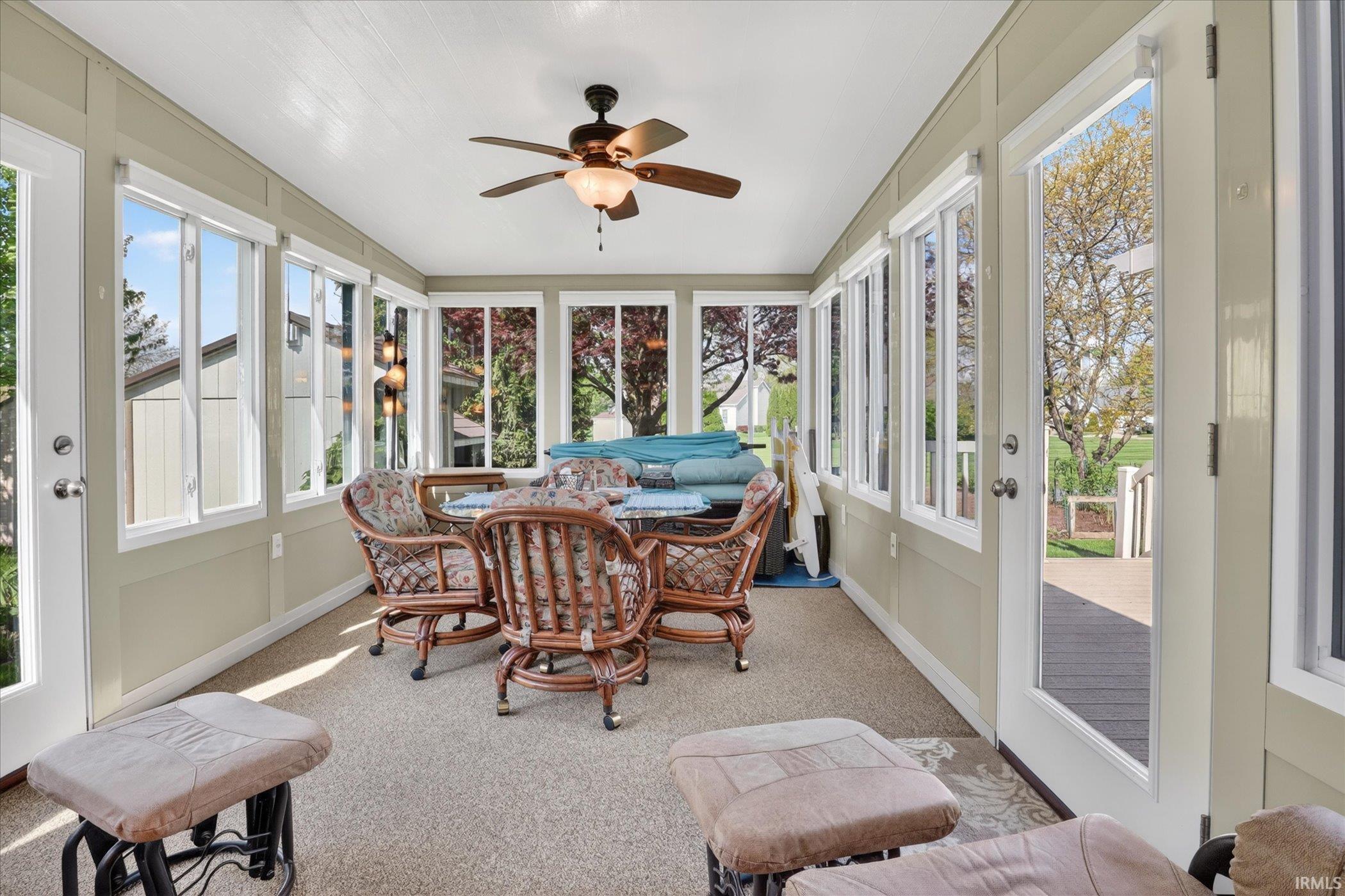 Sunroom featuring walls of windows, two exterior doors, a ceiling fan with integrated lighting, and neutral carpeting