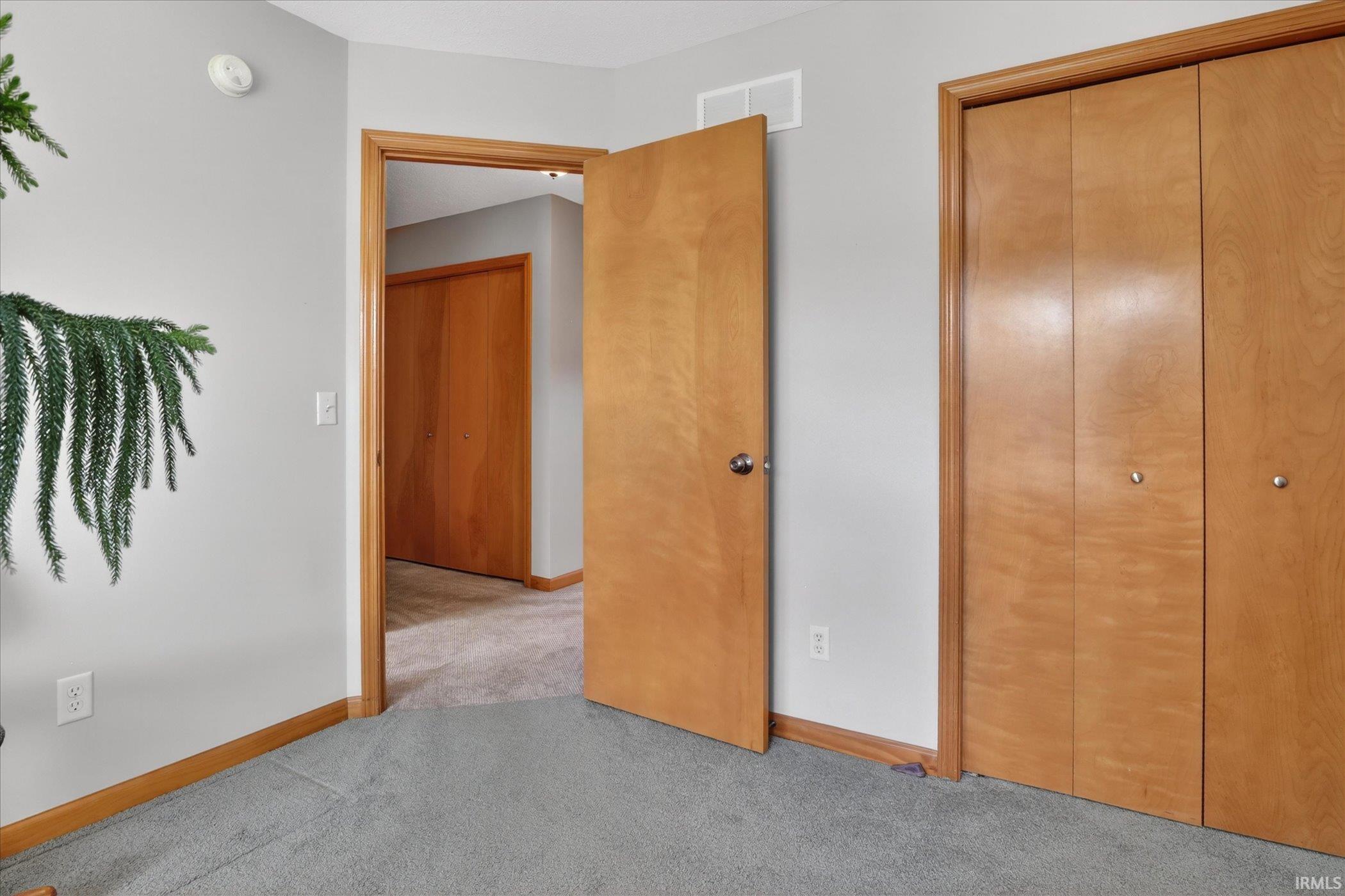 Bedroom featuring light gray walls, carpet flooring, natural wood door frames, and bi-fold closet doors