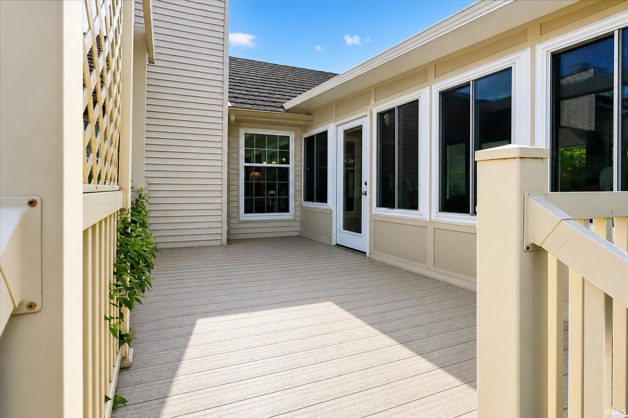 Spacious composite deck featuring privacy lattice, light-colored siding, a full-lite glass door, and multiple pane windows