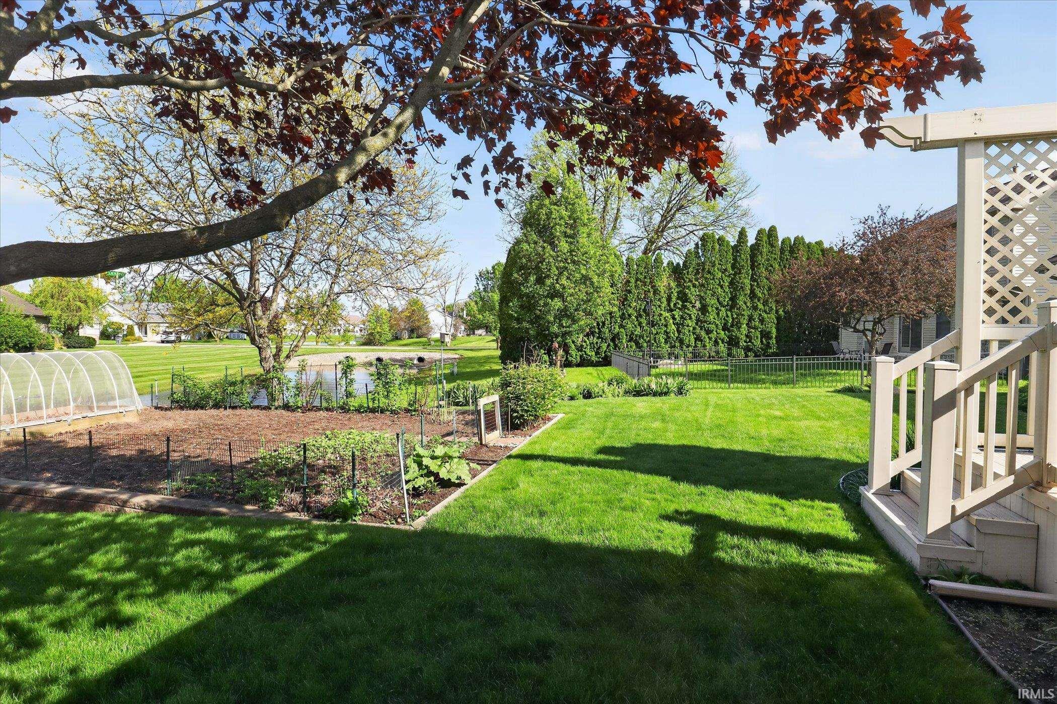 Expansive backyard featuring a manicured lawn, established garden beds, and a functional greenhouse structure