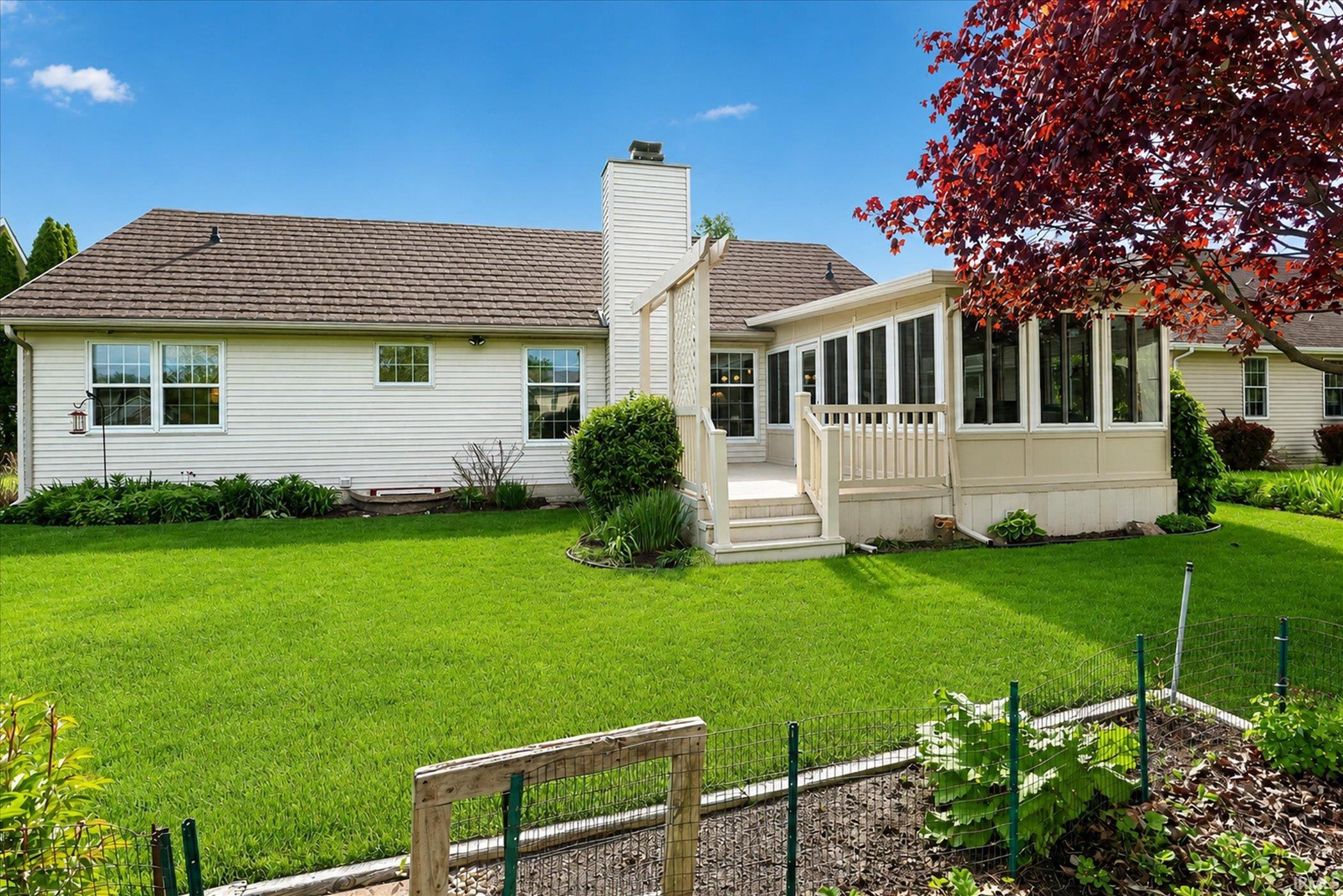 Expansive rear yard featuring a sunroom addition, multi-level deck, and established garden bed
