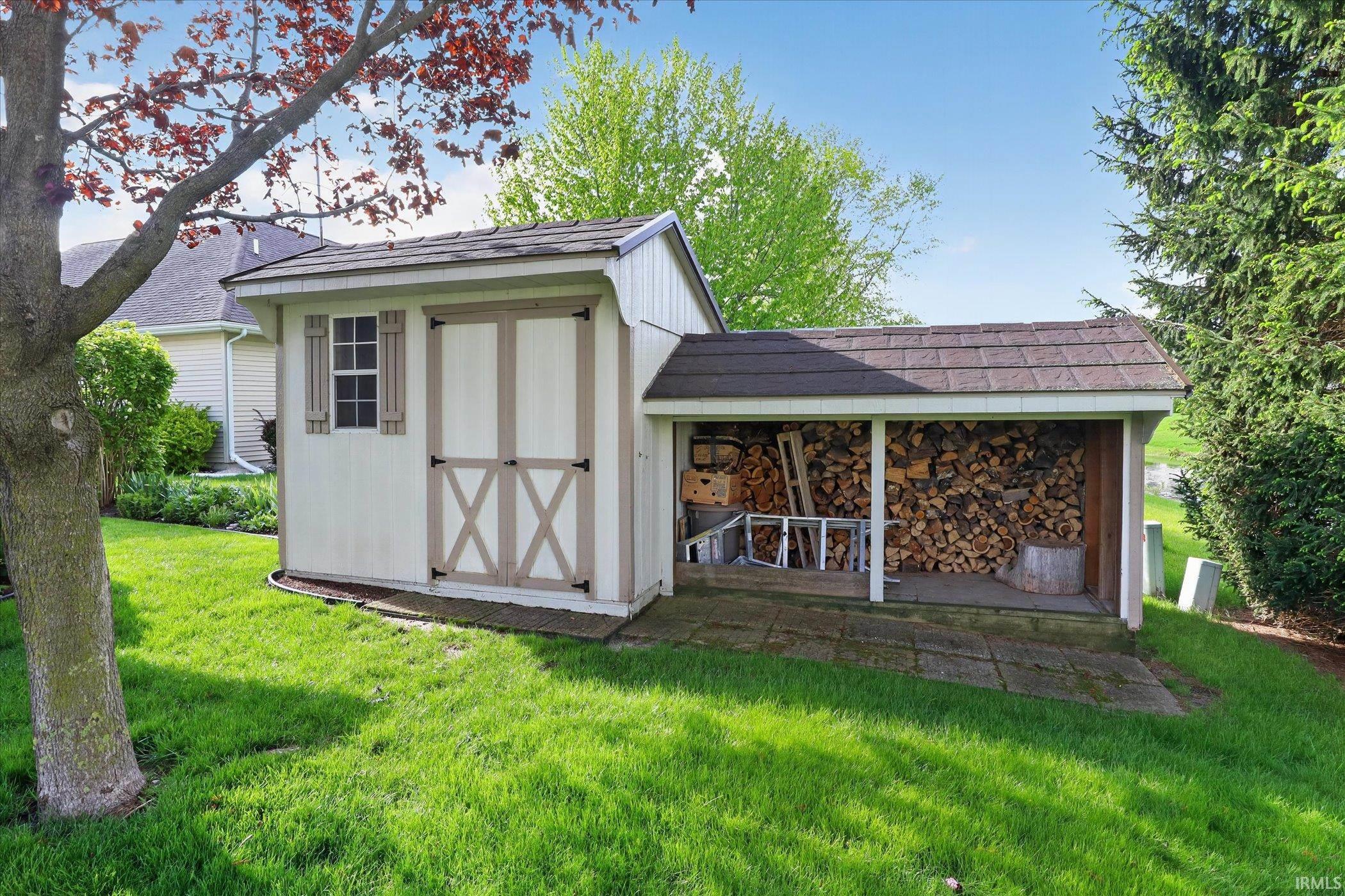 Outdoor storage shed featuring a single window with decorative shutters, double barn-style doors, and an attached covered wood storage area