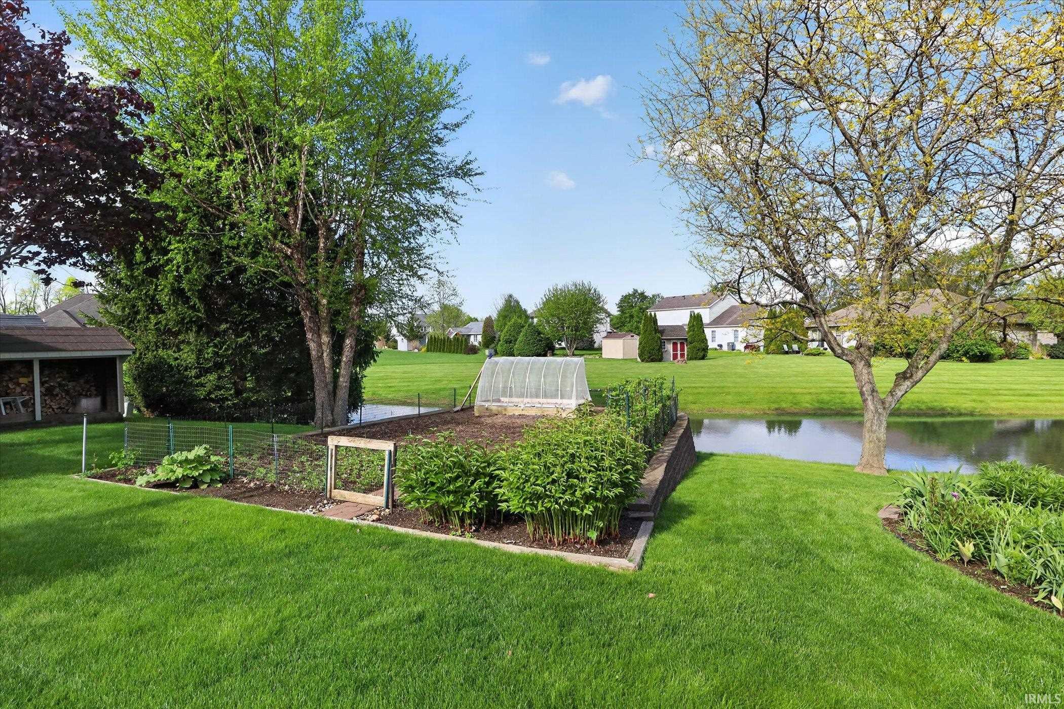 Lush green lawn with a large garden bed, a small greenhouse structure, and a tranquil pond