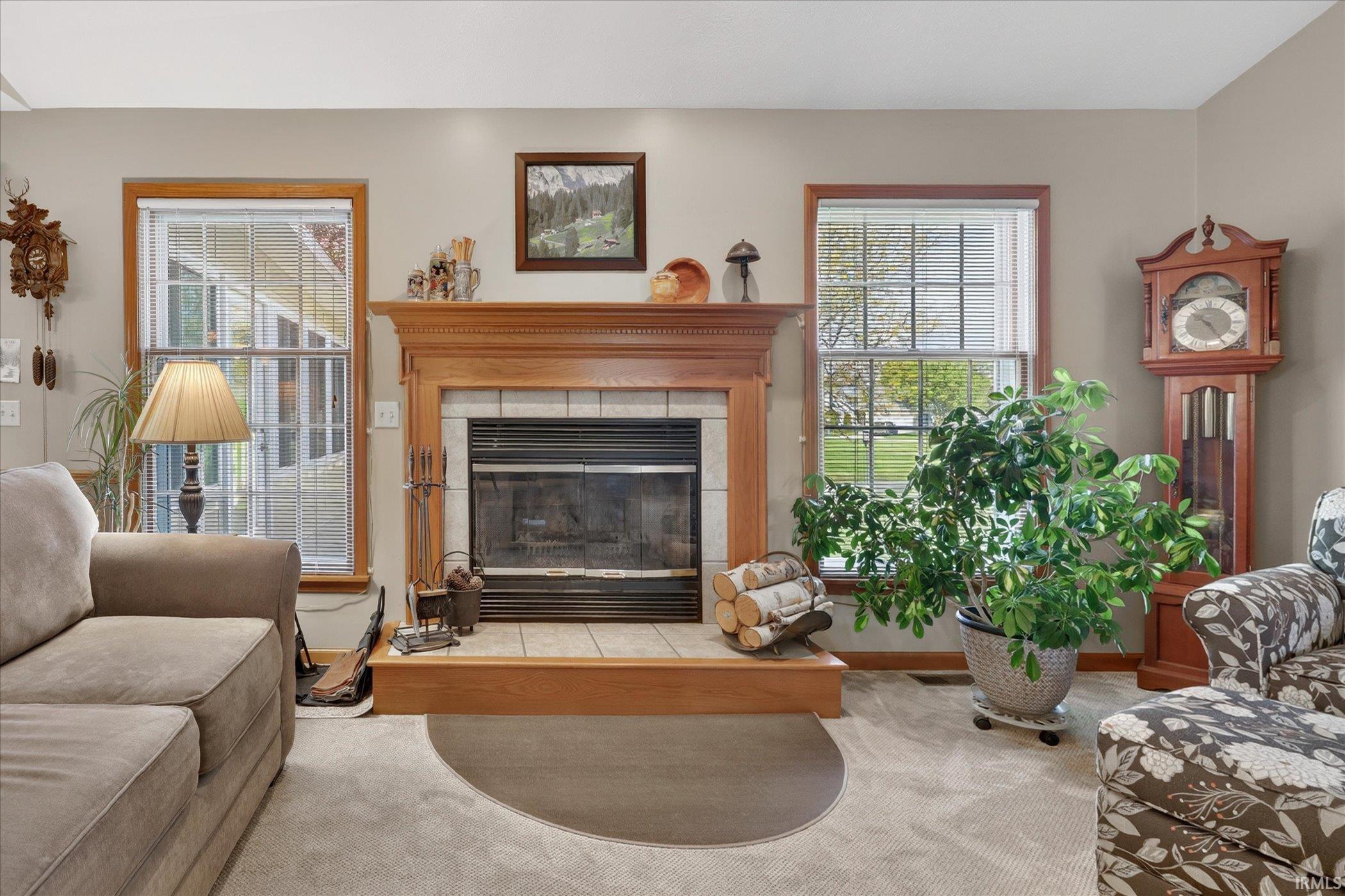 Stone-tiled fireplace with a wood mantle and hearth, flanked by two large windows featuring wood trim