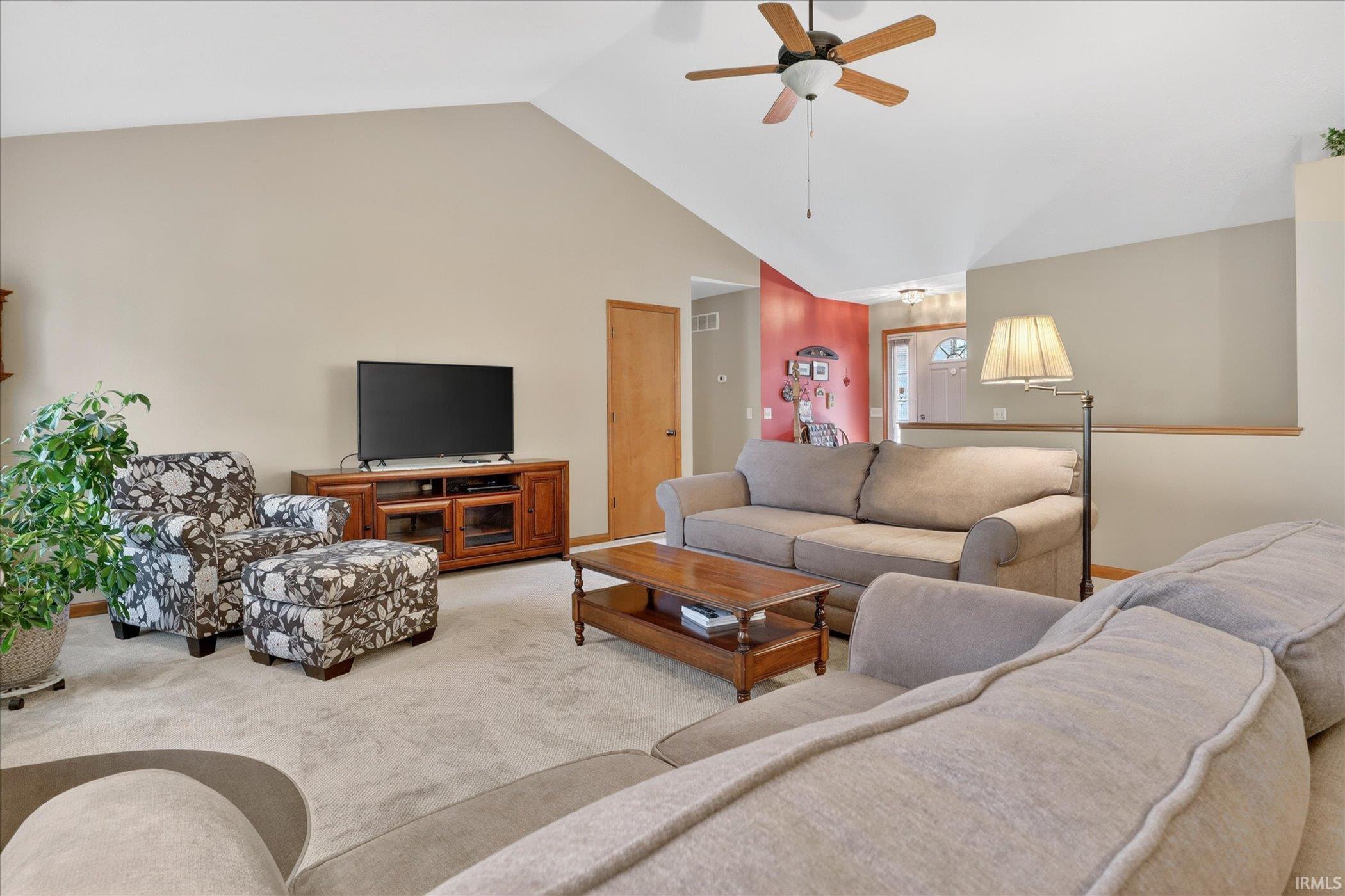 Vaulted ceiling living area featuring a ceiling fan, carpet flooring, and a wood-finish media console